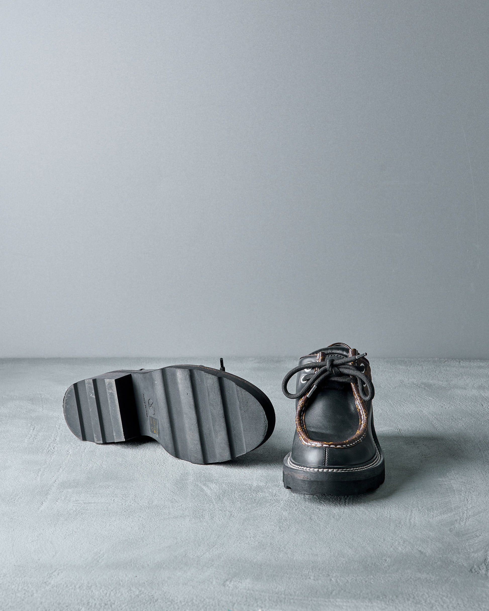 Black leather Louis Vuitton shoes on a gray surface with a neutral background