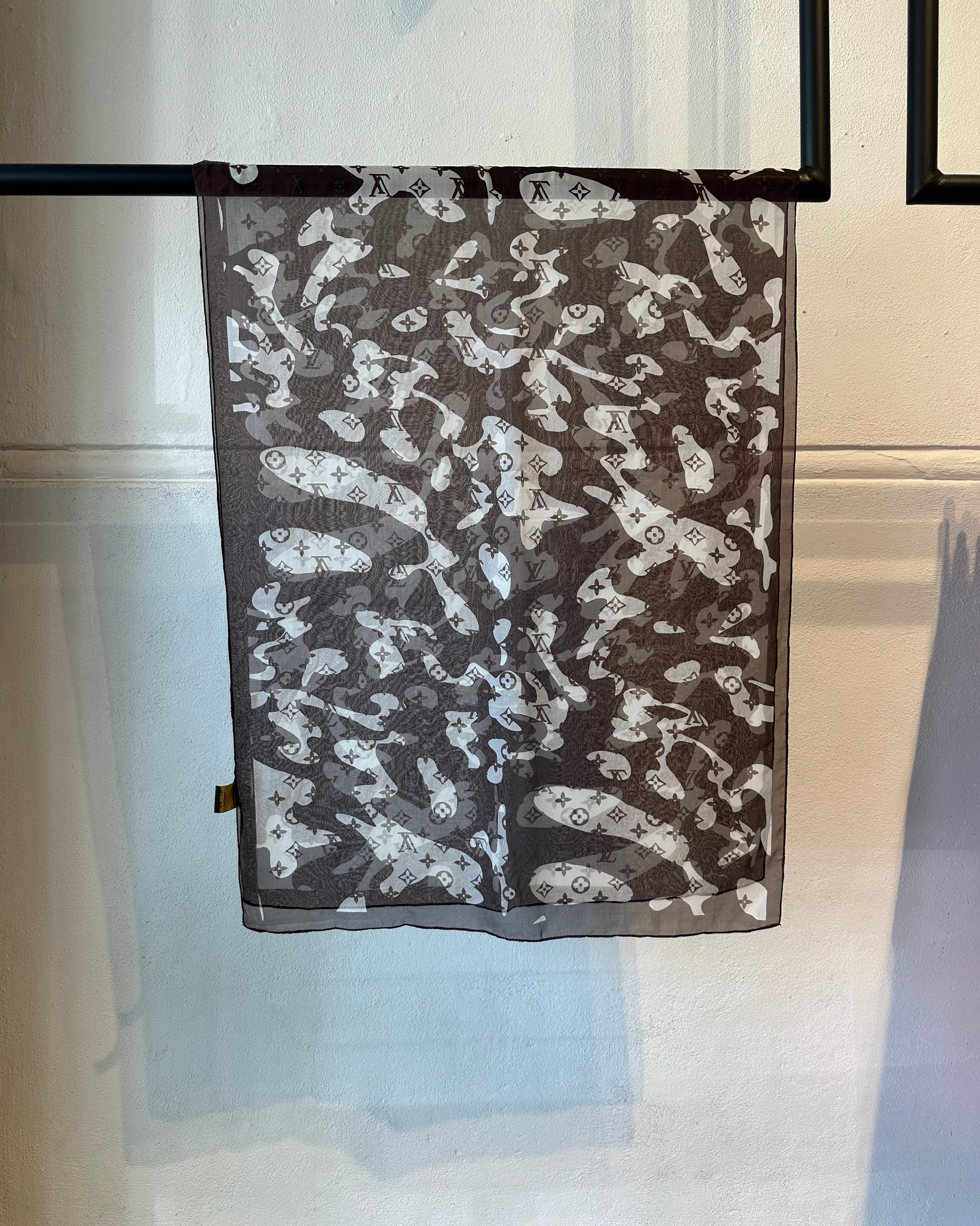 Brown patterned  Louis Vuitton scarf on a hanger against a neutral background