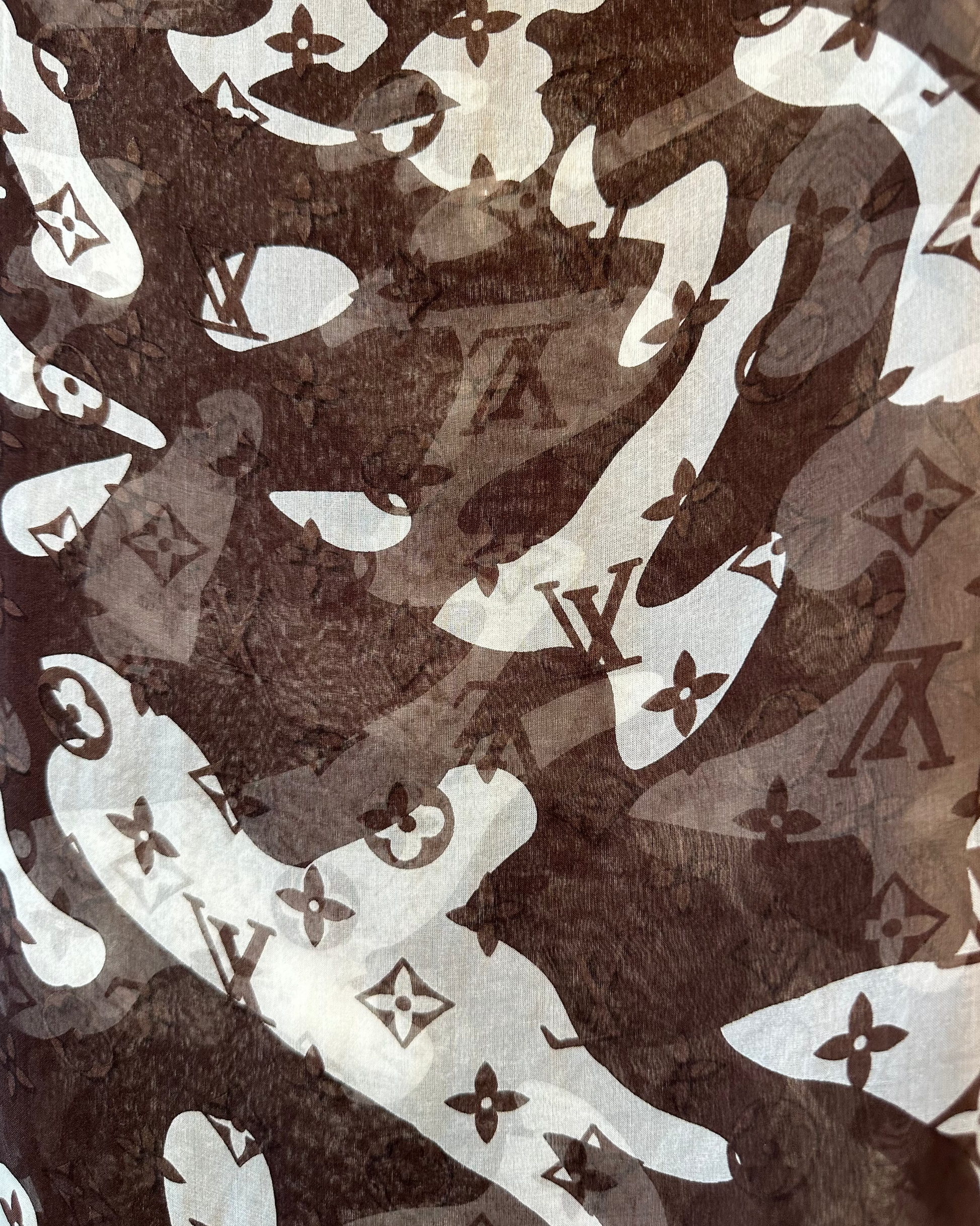 Patterned fabric of a brown and white Louis Vuitton scarf with brand logos and abstract shapes