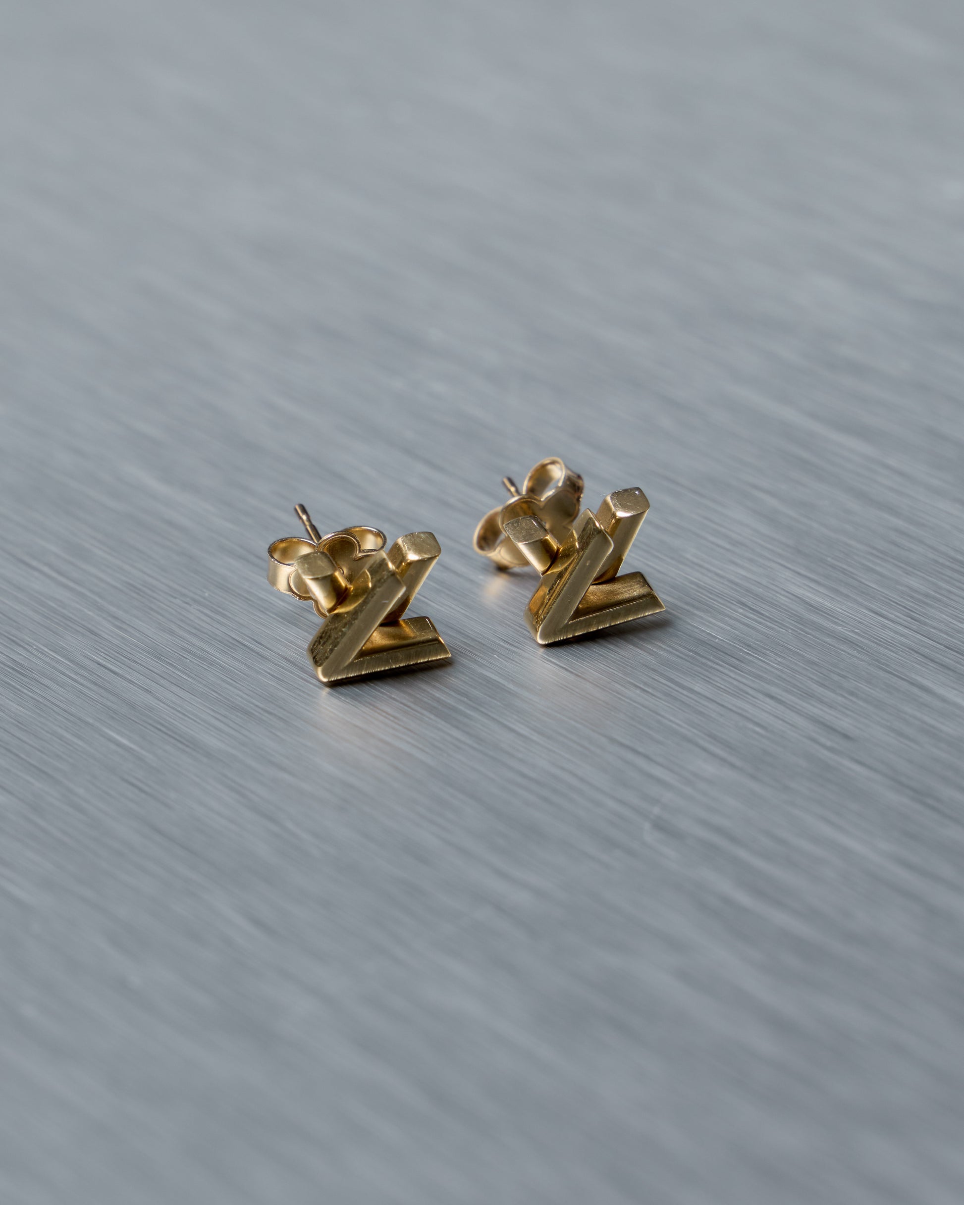 Pair of gold Louis Vuitton earrings on a textured gray surface