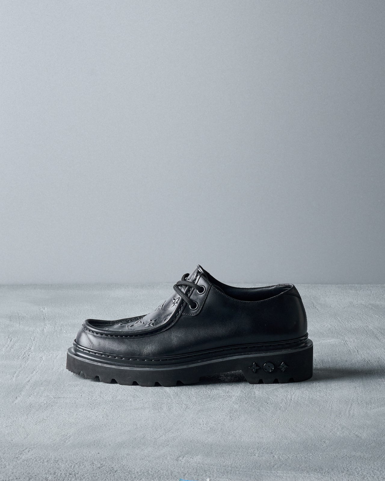 Black leather Louis Vuitton shoe on a gray surface with a gray background