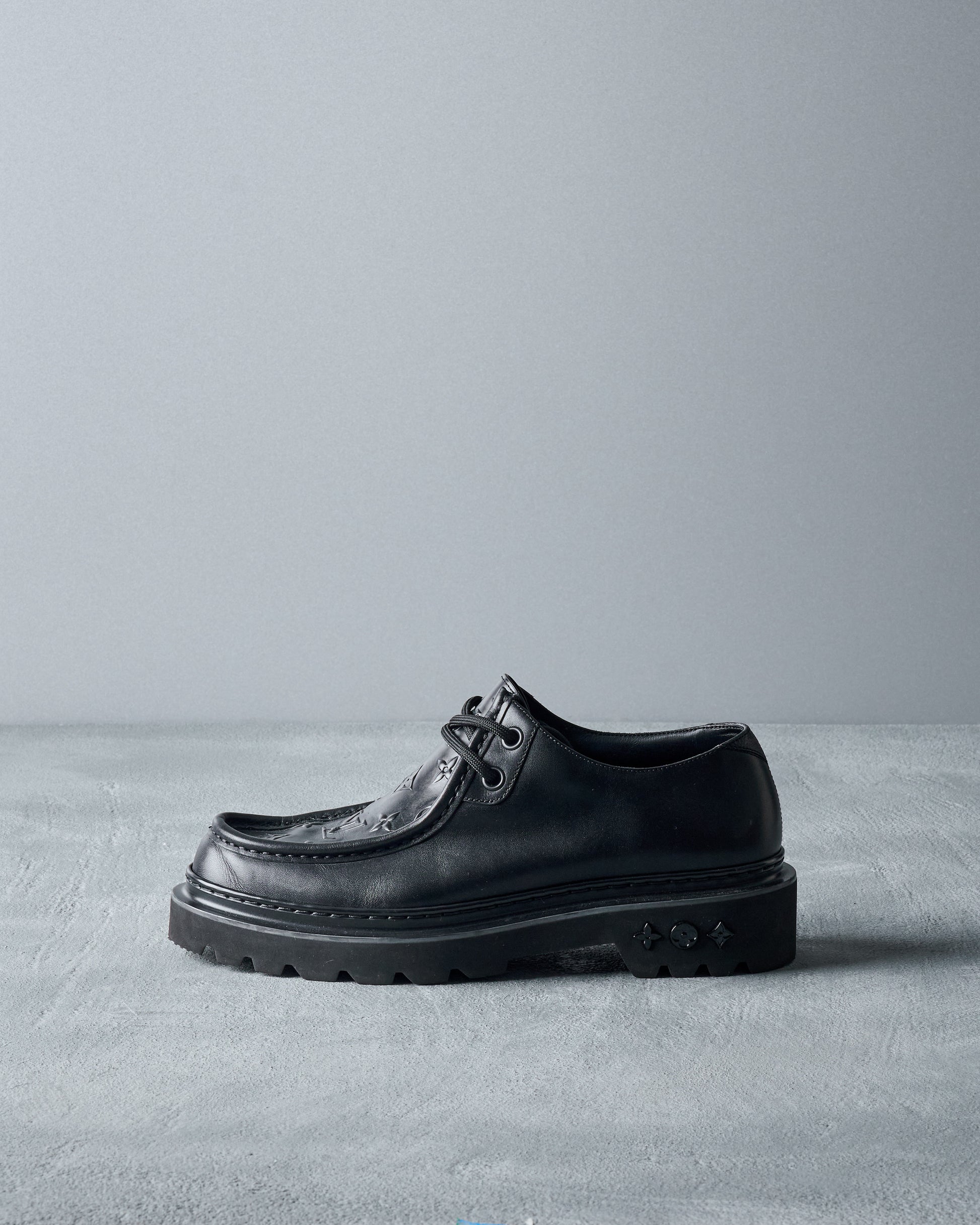 Black leather Louis Vuitton shoe on a gray surface with a gray background
