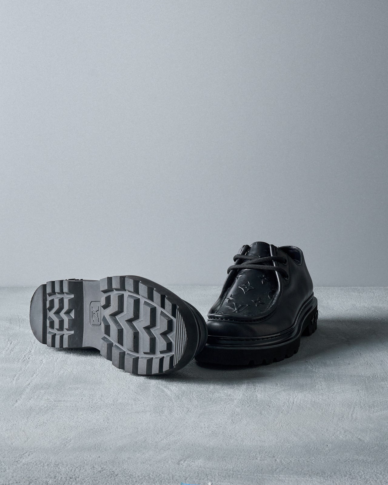 Black leather Louis Vuitton shoe on a gray surface with a gray background