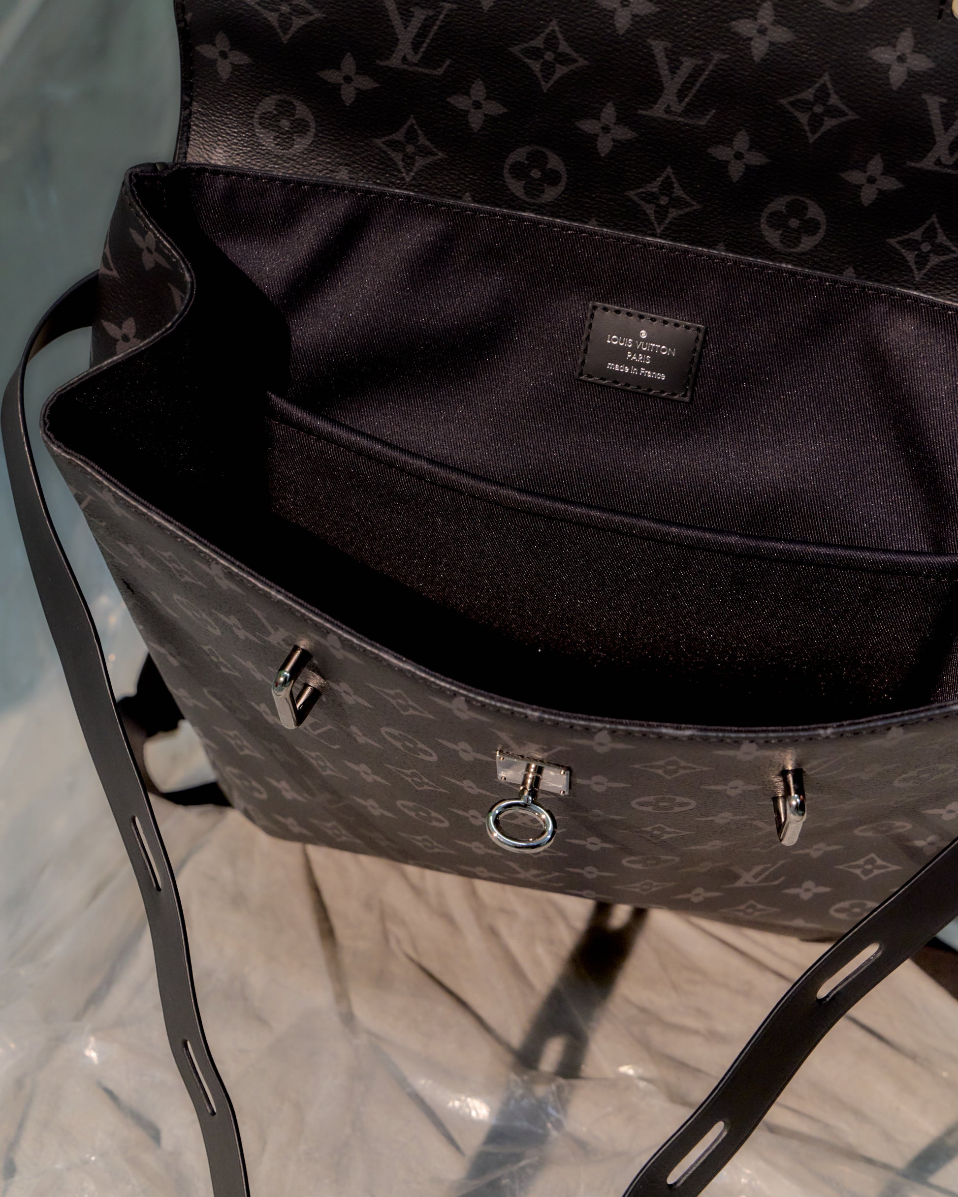 Close-up of a black Louis Vuitton backpack with a monogram pattern on a reflective surface