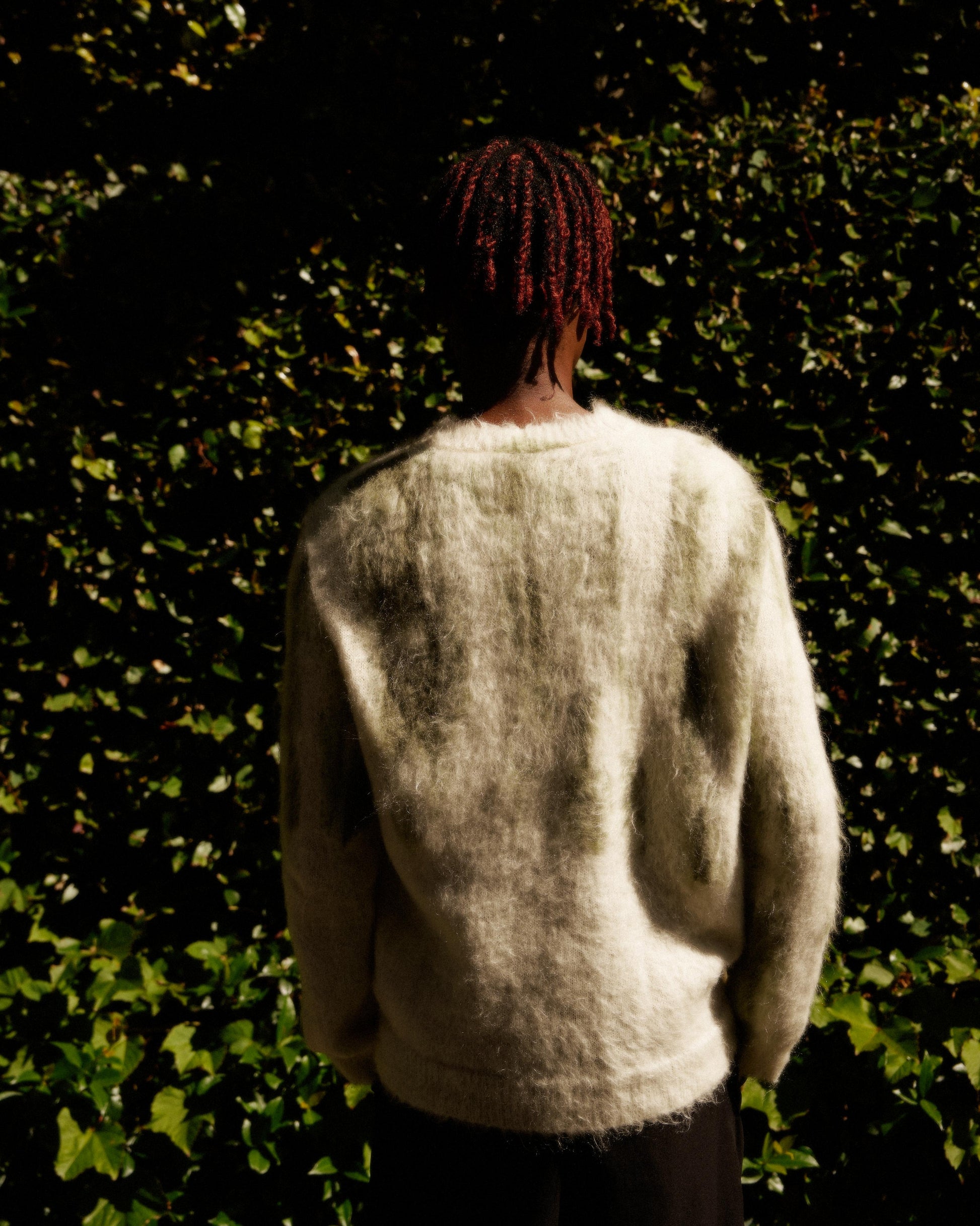 Person with red braided hair stands with their back to the camera, wearing a fuzzy cream Louis Vuitton sweater.