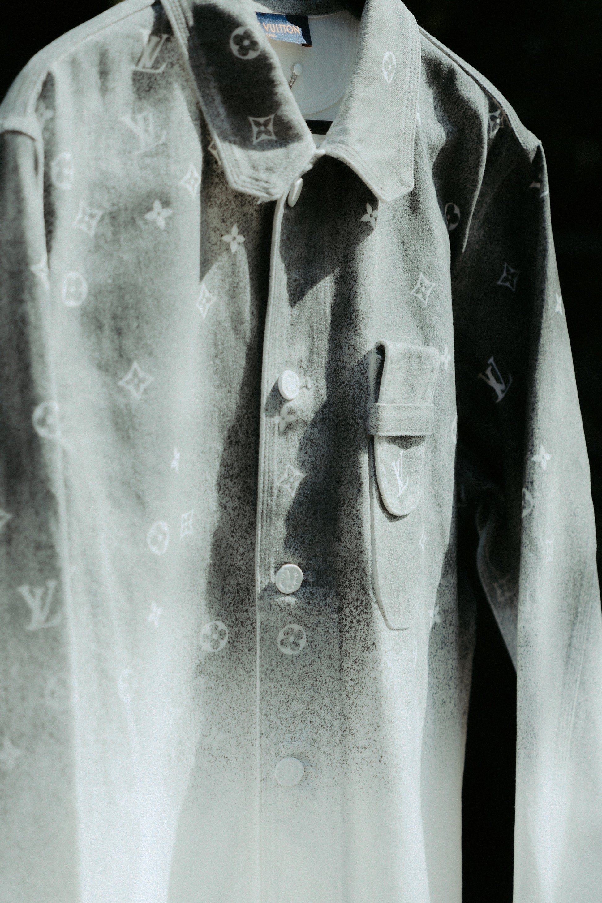 Close-up of a designer Louis Vuitton jacket with a textured gray and white gradient, featuring a subtle monogram pattern. 