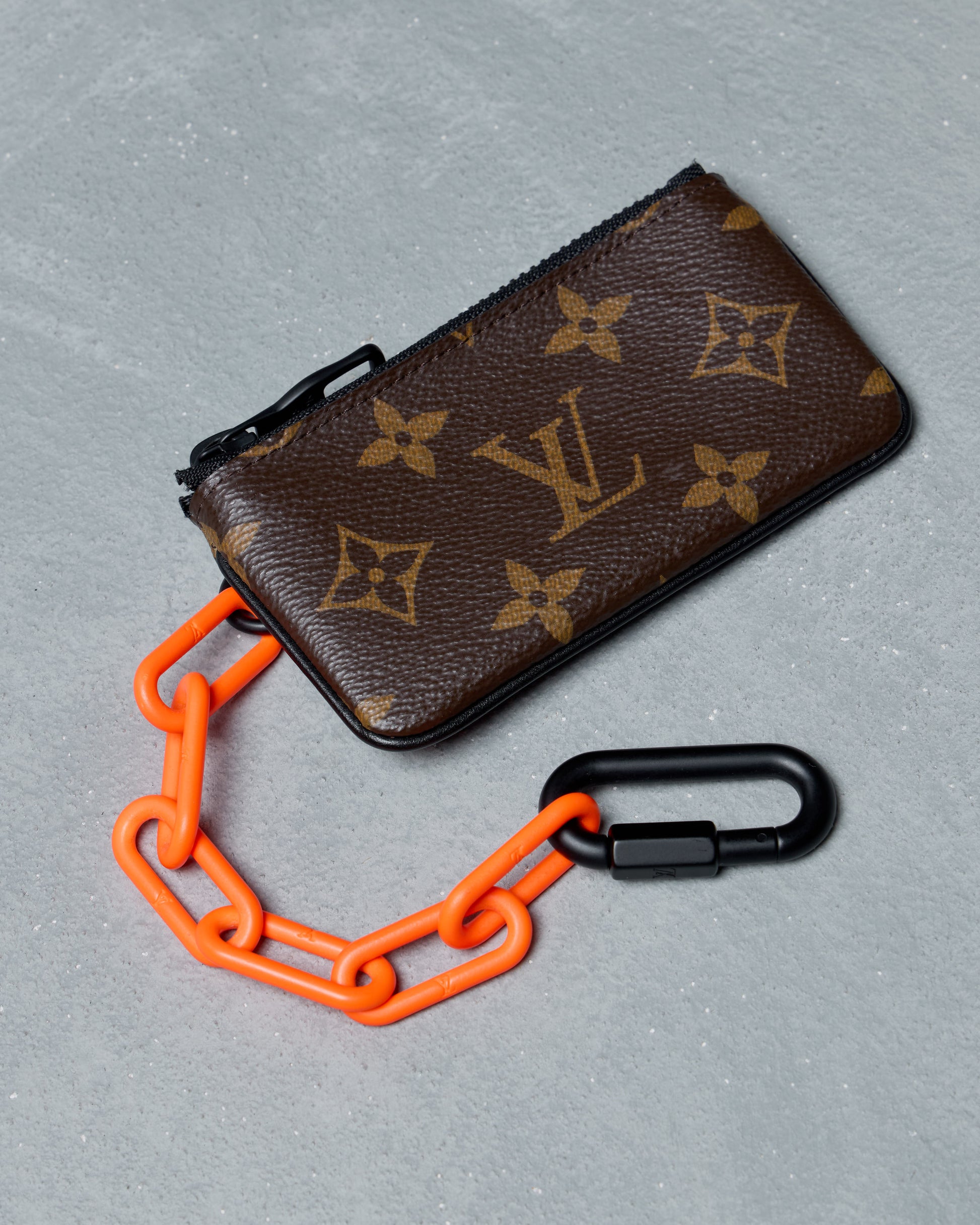 Louis Vuitton key pouch with orange chain on a gray background
