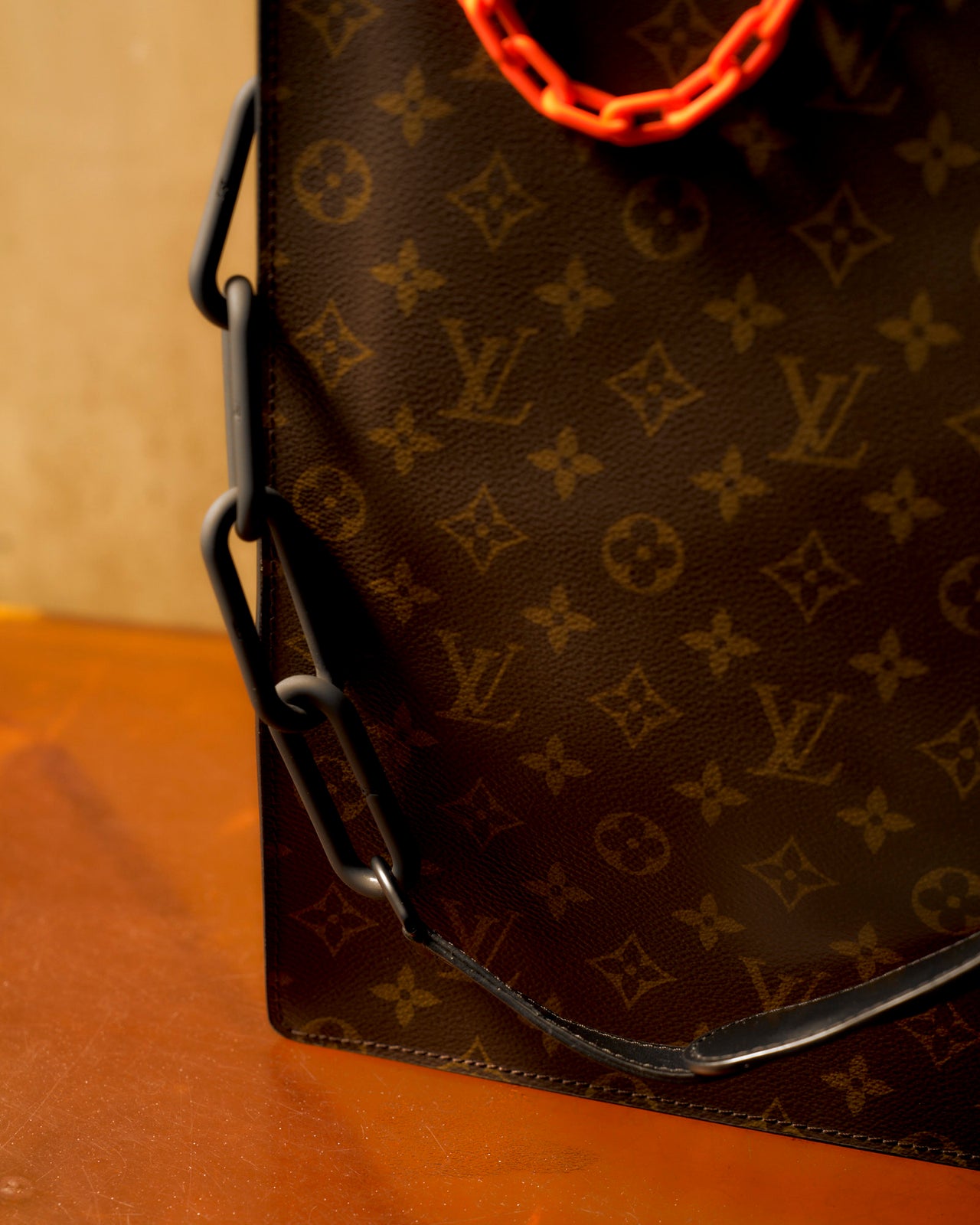 Louis Vuitton monogram tote bag with orange chain, matte black leather detailing, and a visible logo on the fabric.