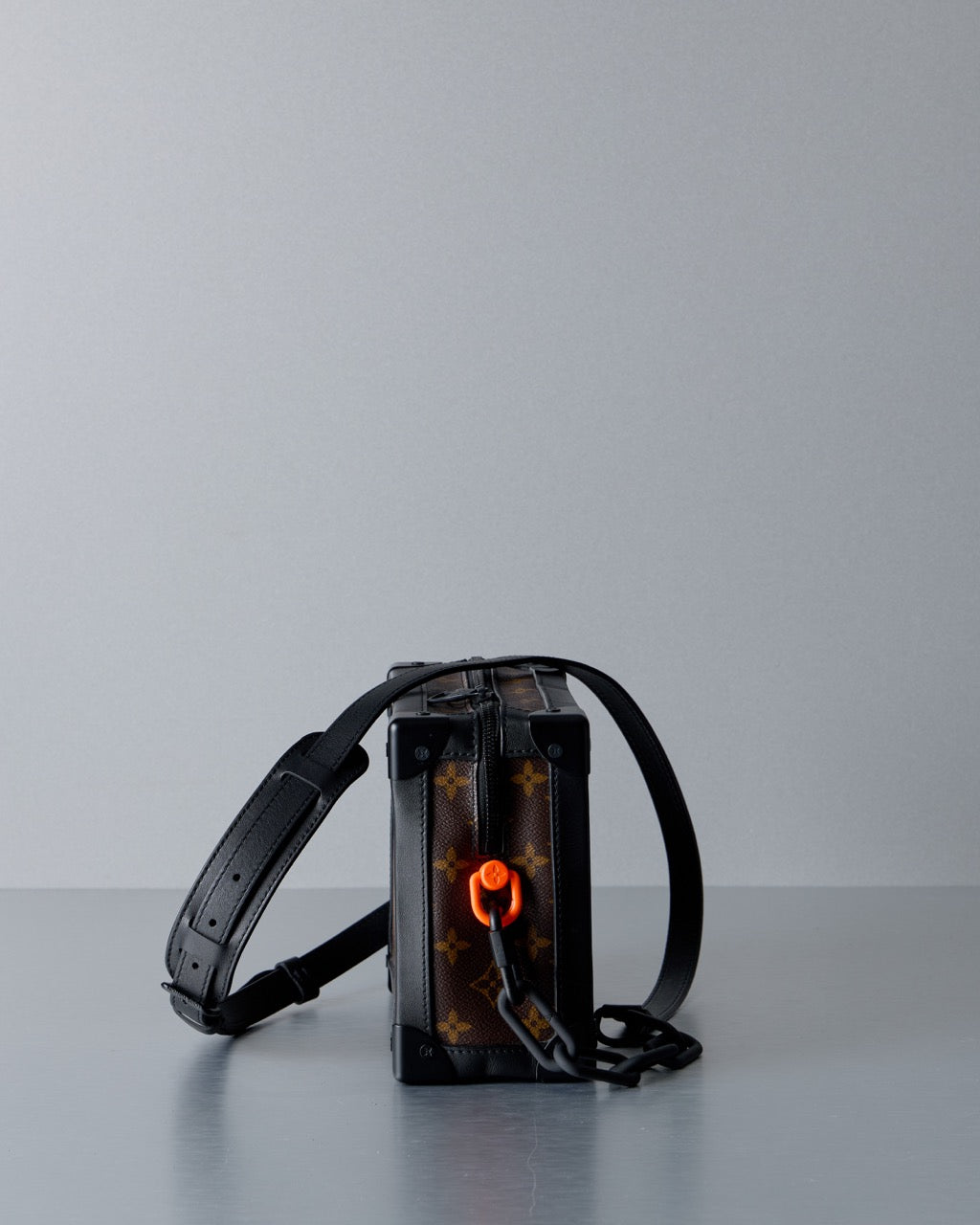 Small black rectangular Louis Vuitton bag with a strap on a gray surface and light gray background