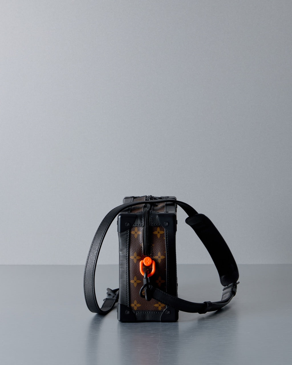 Black Louis Vuitton cross body bag with reflective materials on a gray background