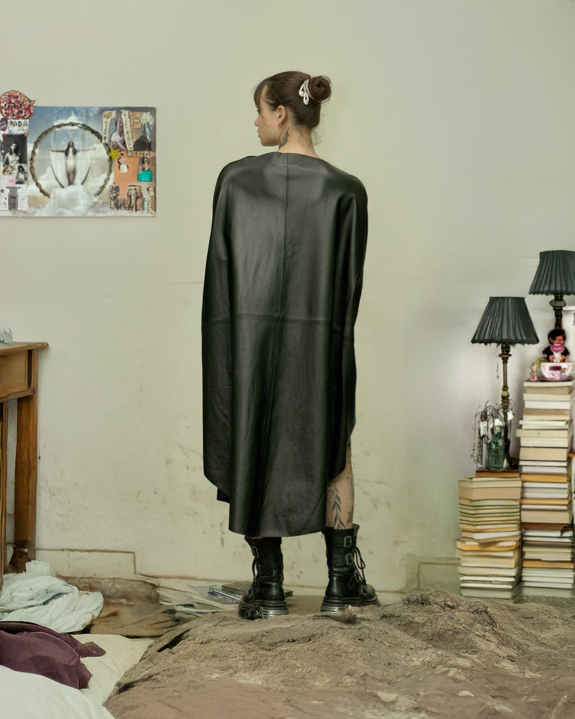 Person wearing a black leather MM6 Maison Margiela dress in a room with books and a lamp.