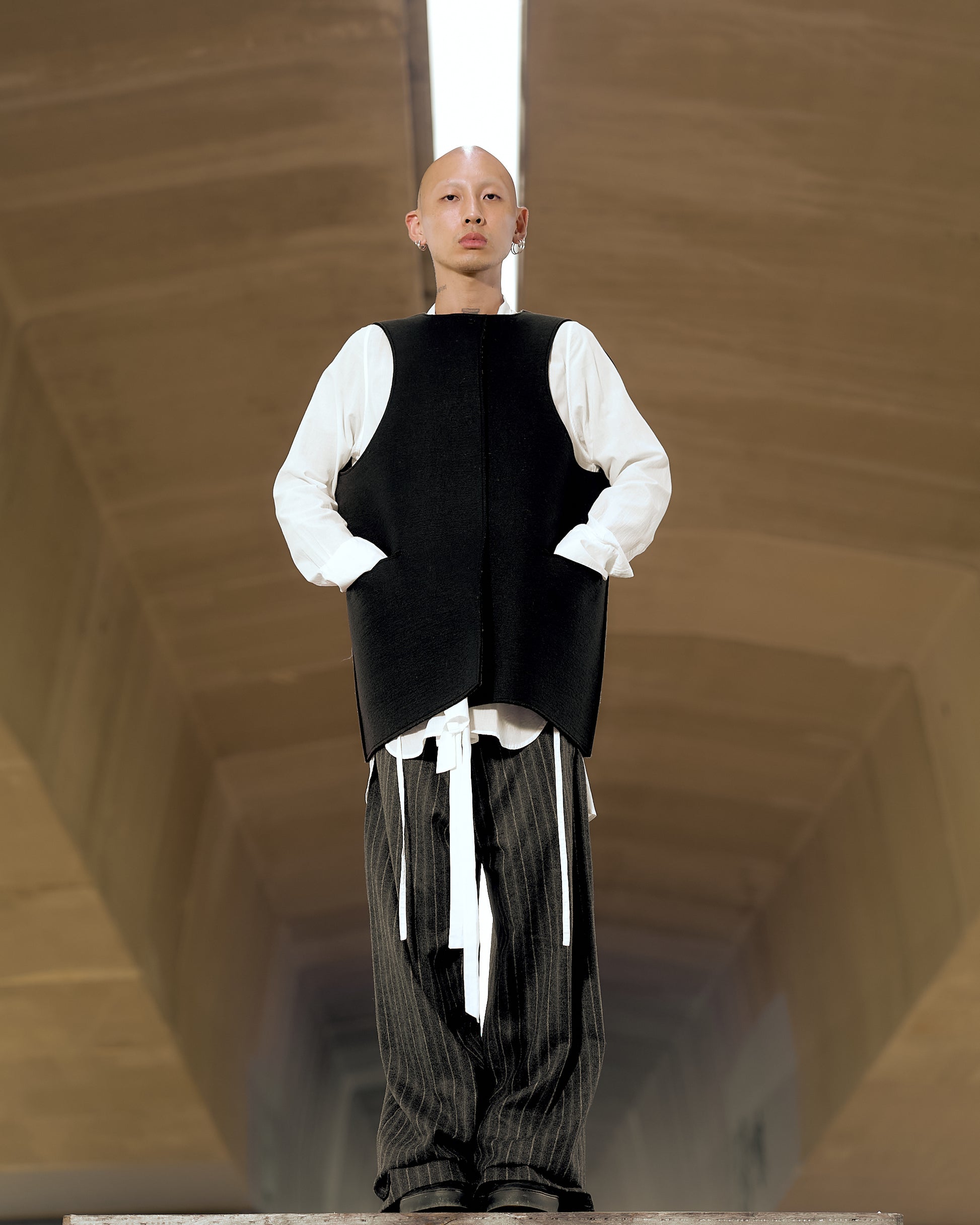 A model wearing a black Maison Margiela artistic vest with a large collar, press stud closures, and hip pockets.
