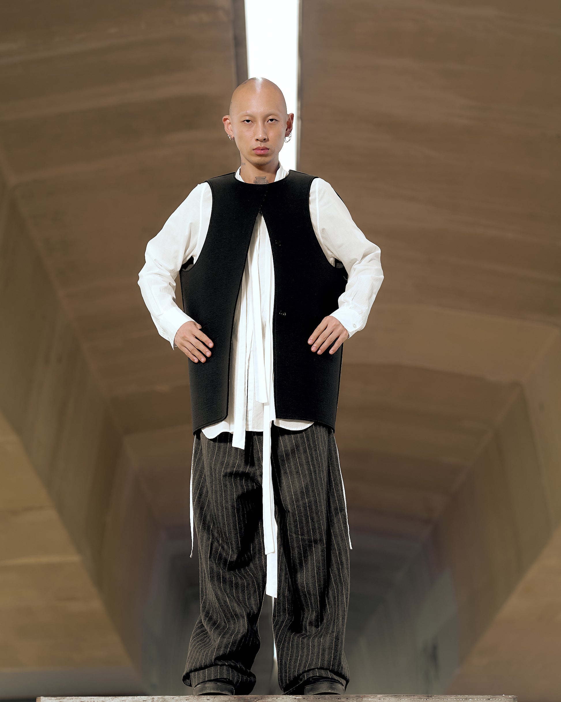 A person wearing a Maison Margiela 1998 Artisanal 'flat pattern' bonded felt vest with a white shirt and striped trousers.