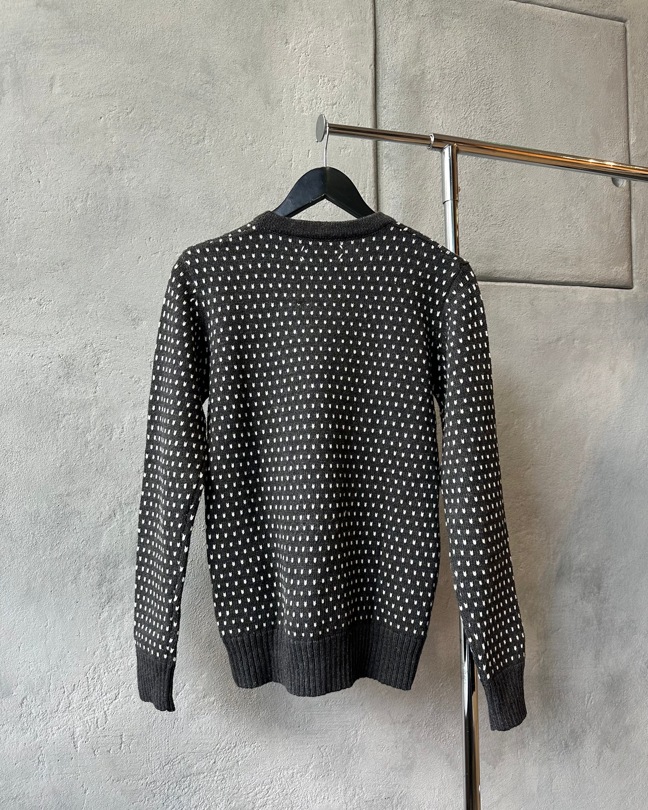 Charcoal Maison Margiela sweater with white pattern on a hanger against a gray wall