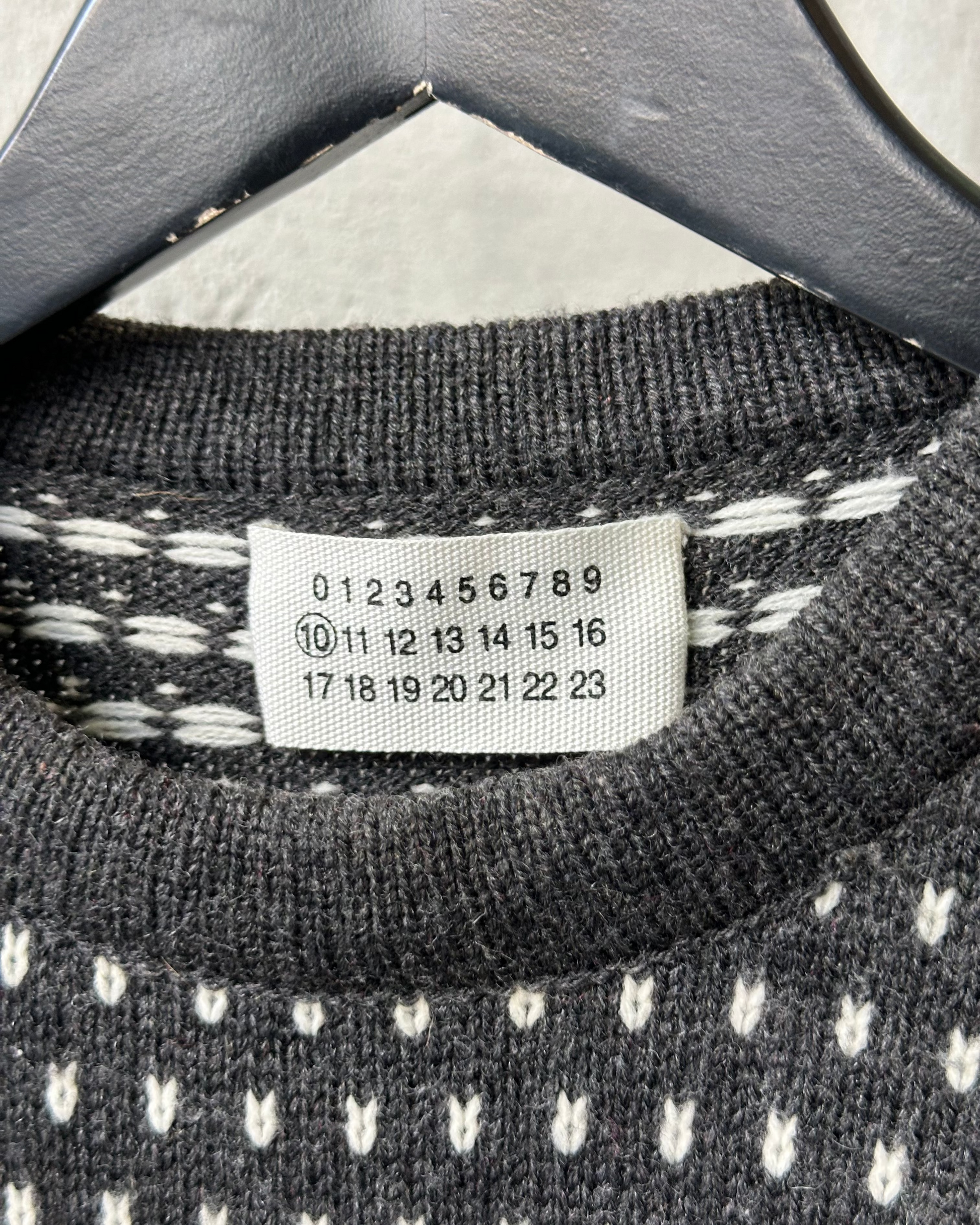 Close-up of a Maison Margiela label on a black and white patterned garment with a hanger.
