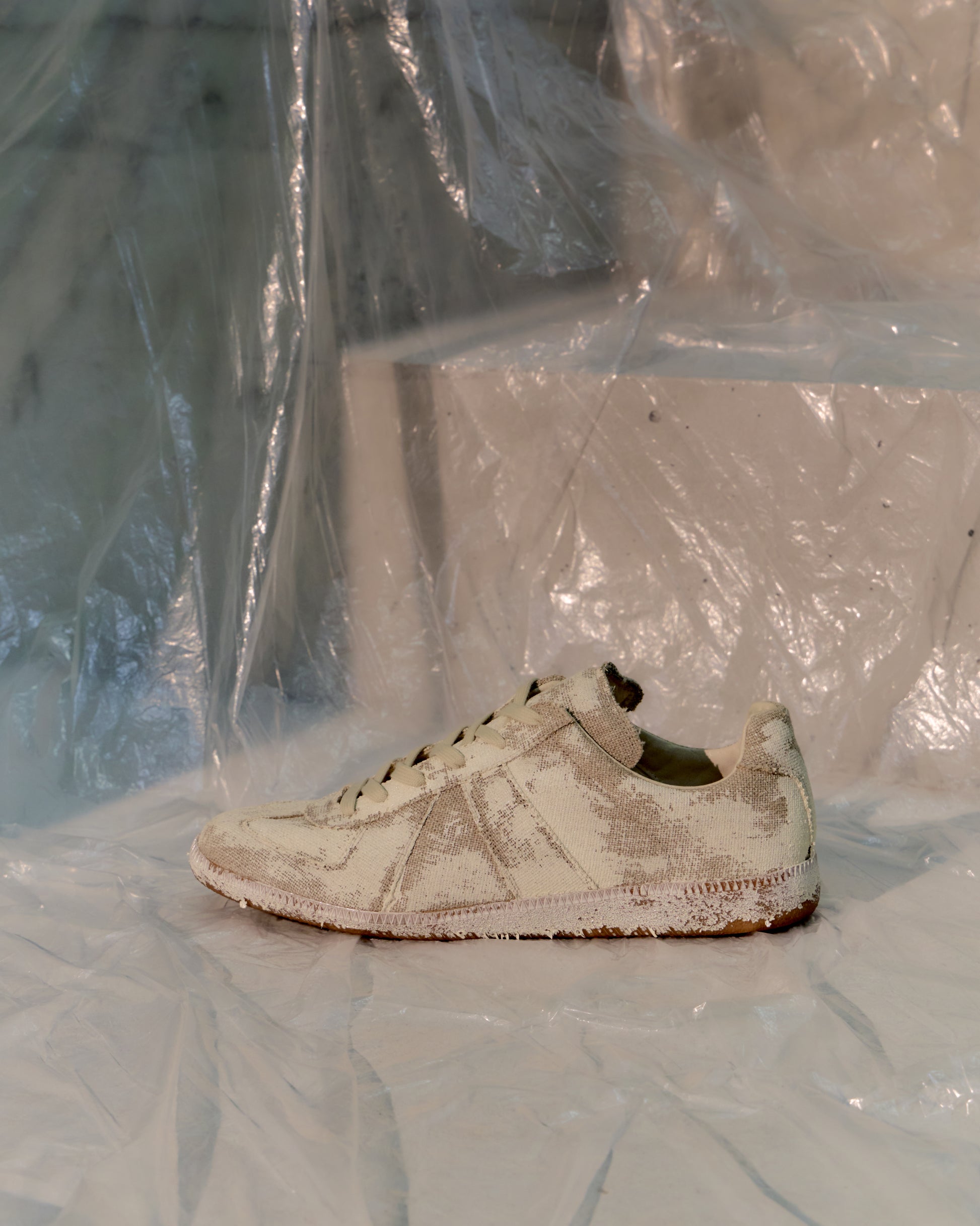 White Maison Margiela GAT sneaker with visible wear on a white surface with plastic sheeting in the background