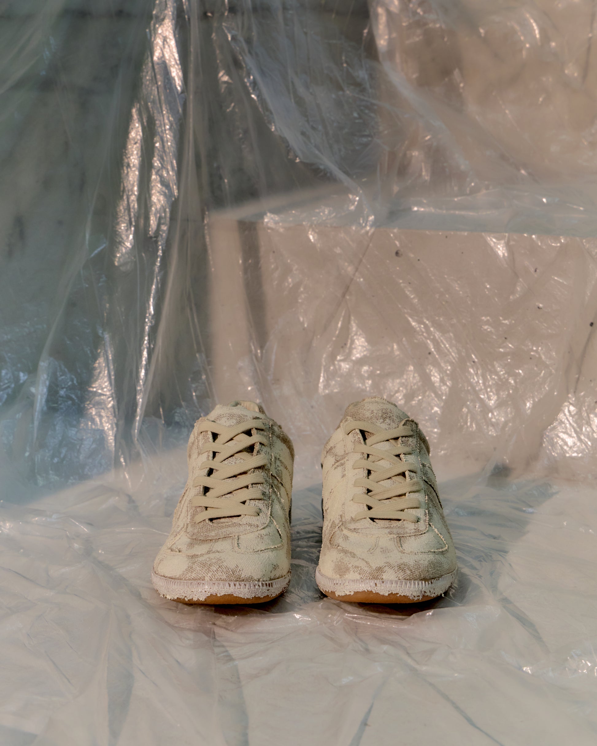 Pair of white Maison Margiela GAT sneakers on a surface with plastic sheeting in the background