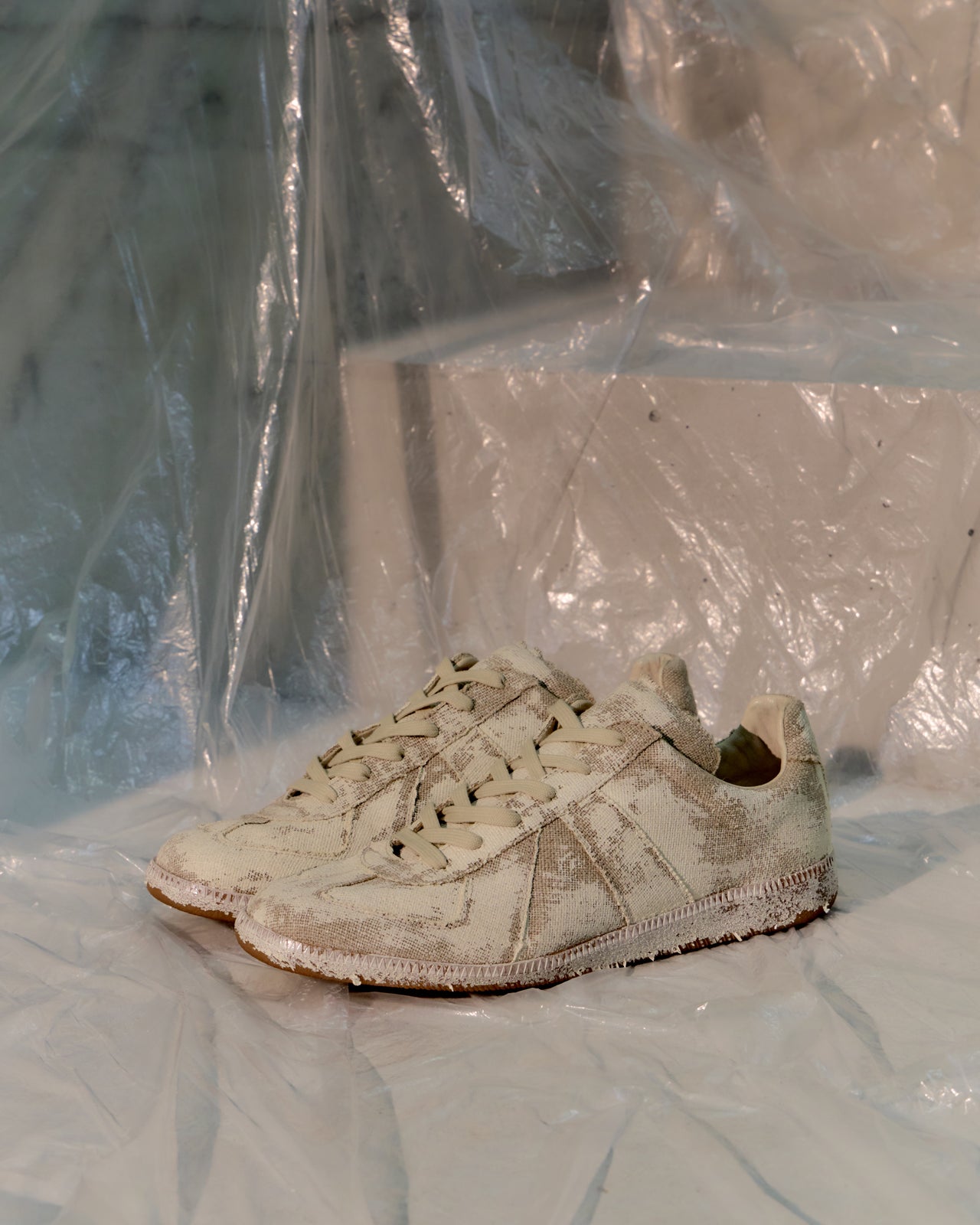 White Maison Margiela GAT sneaker with visible wear on a white surface with plastic sheeting in the background