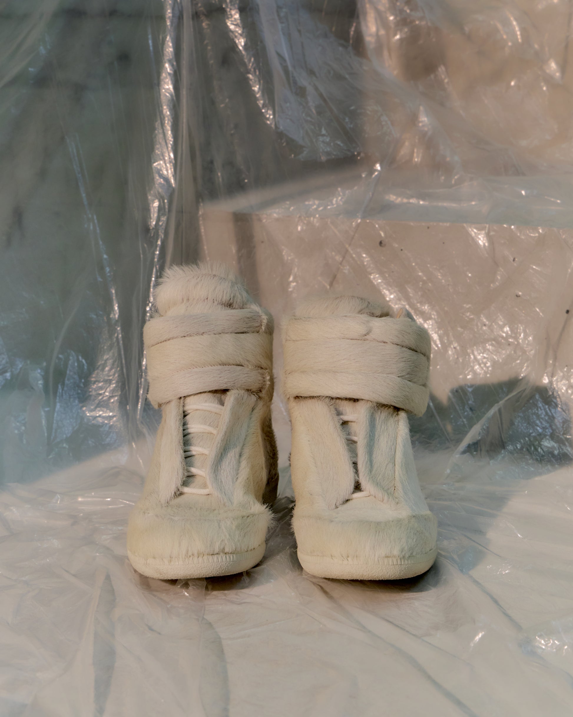 White Maison Margiela high-top sneakers on a white surface with a clear plastic sheet in the background