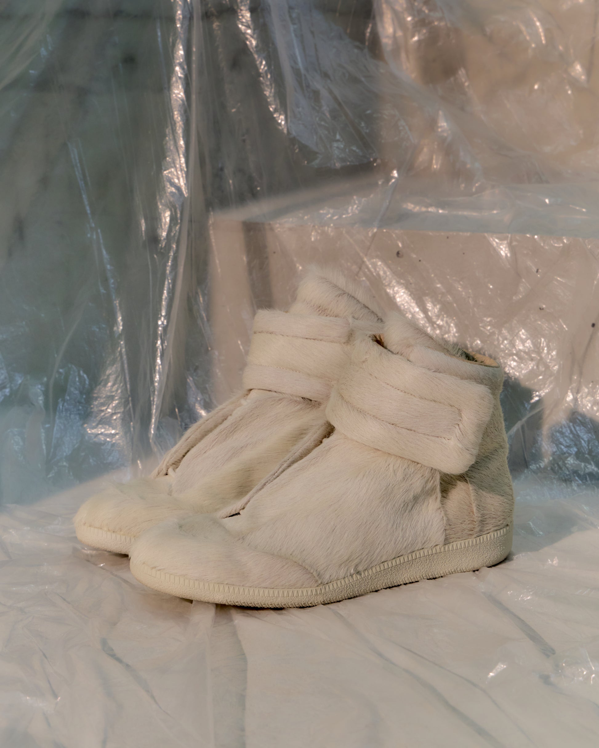 White Maison Margiela wedge sneakers on a white surface with a clear plastic sheet in the background
