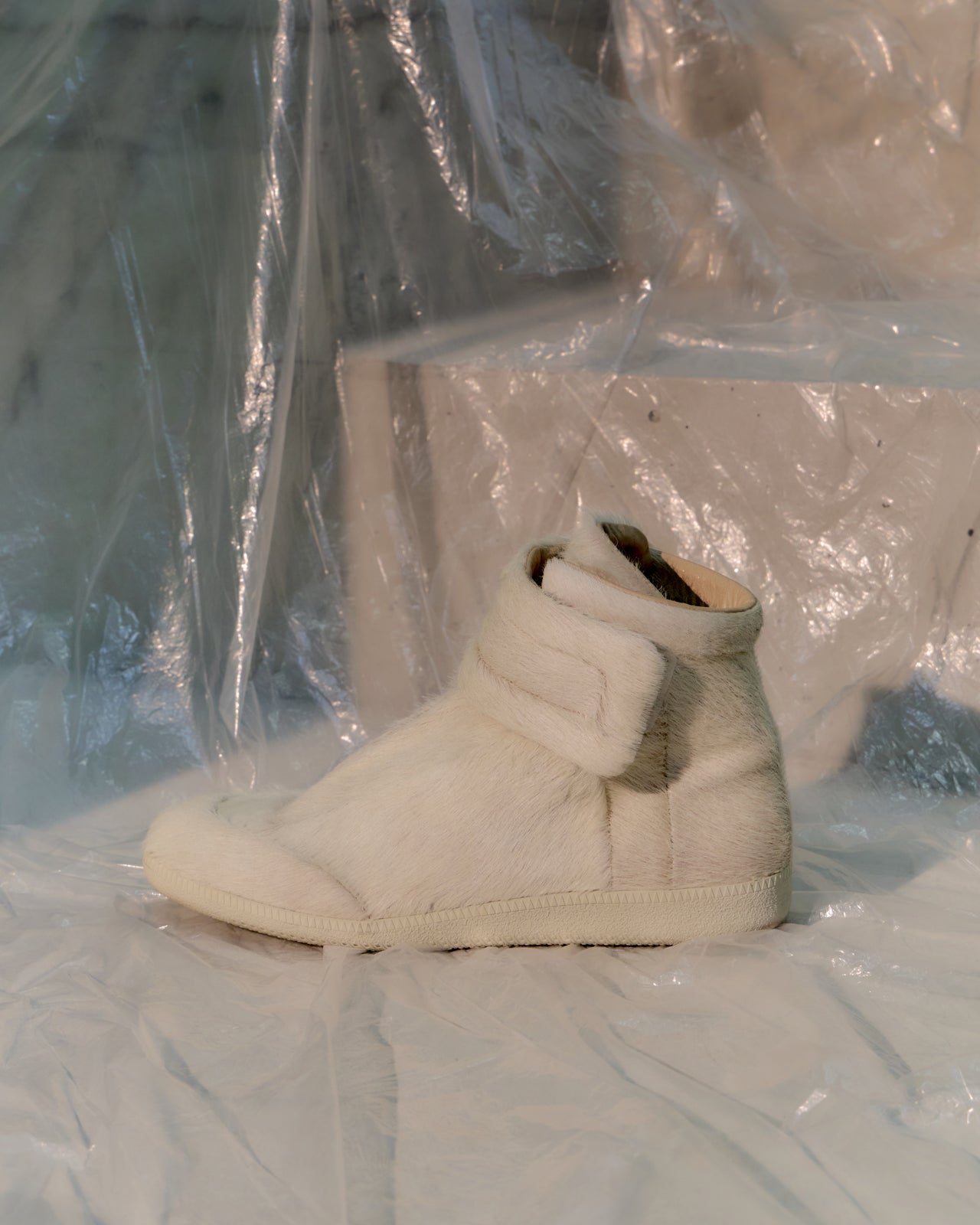 White high-top Maison Margiela sneakers on a white surface with plastic wrap in the background