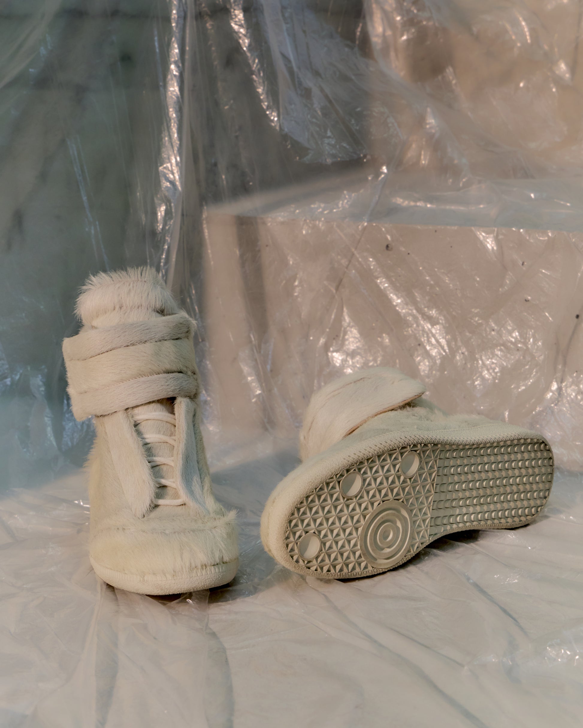 Pair of white Maison Margiela high-top sneakers on a white surface with a plastic sheet in the background