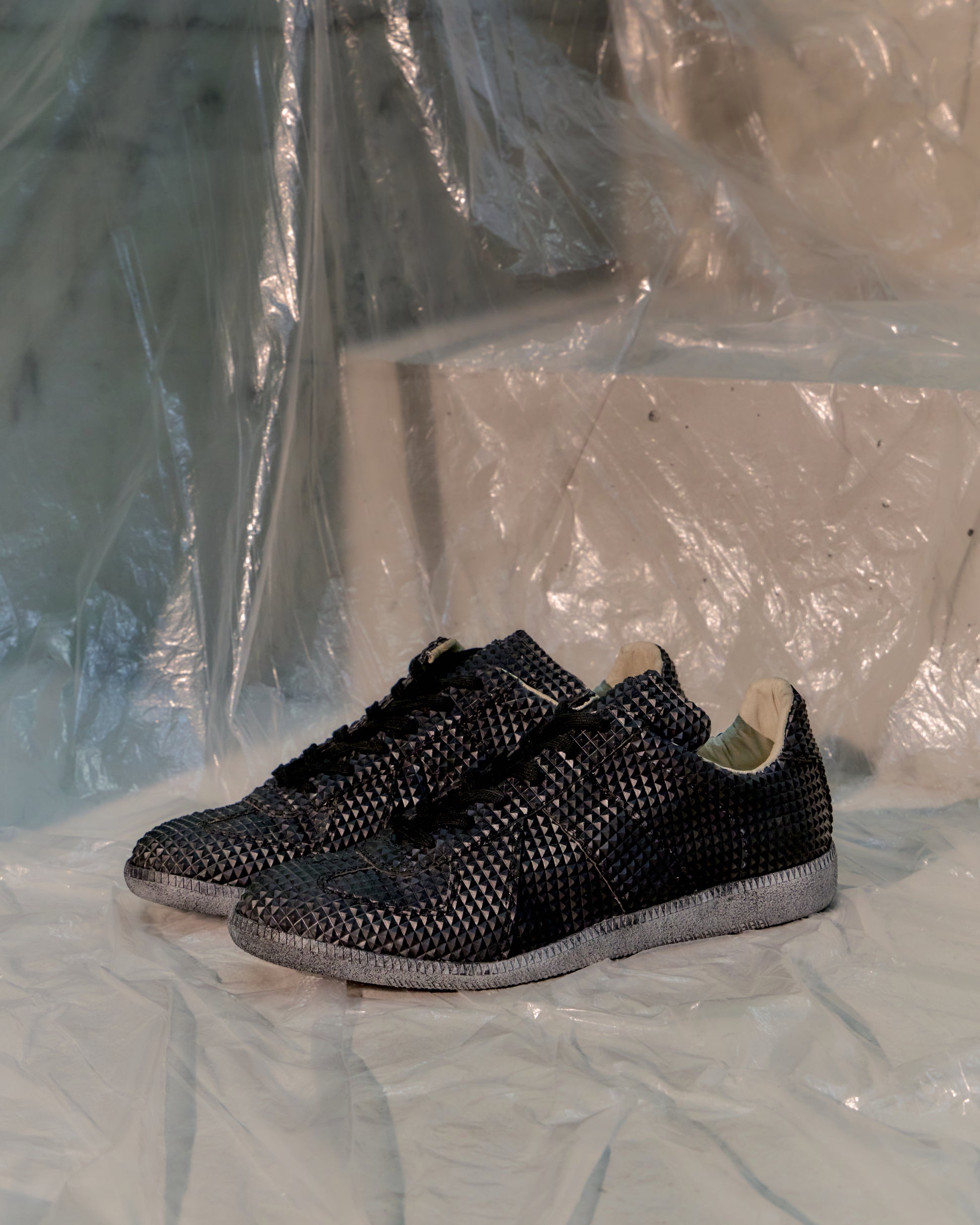 Black woven Maison Margiela GAT sneakers on a white surface with a plastic sheet background