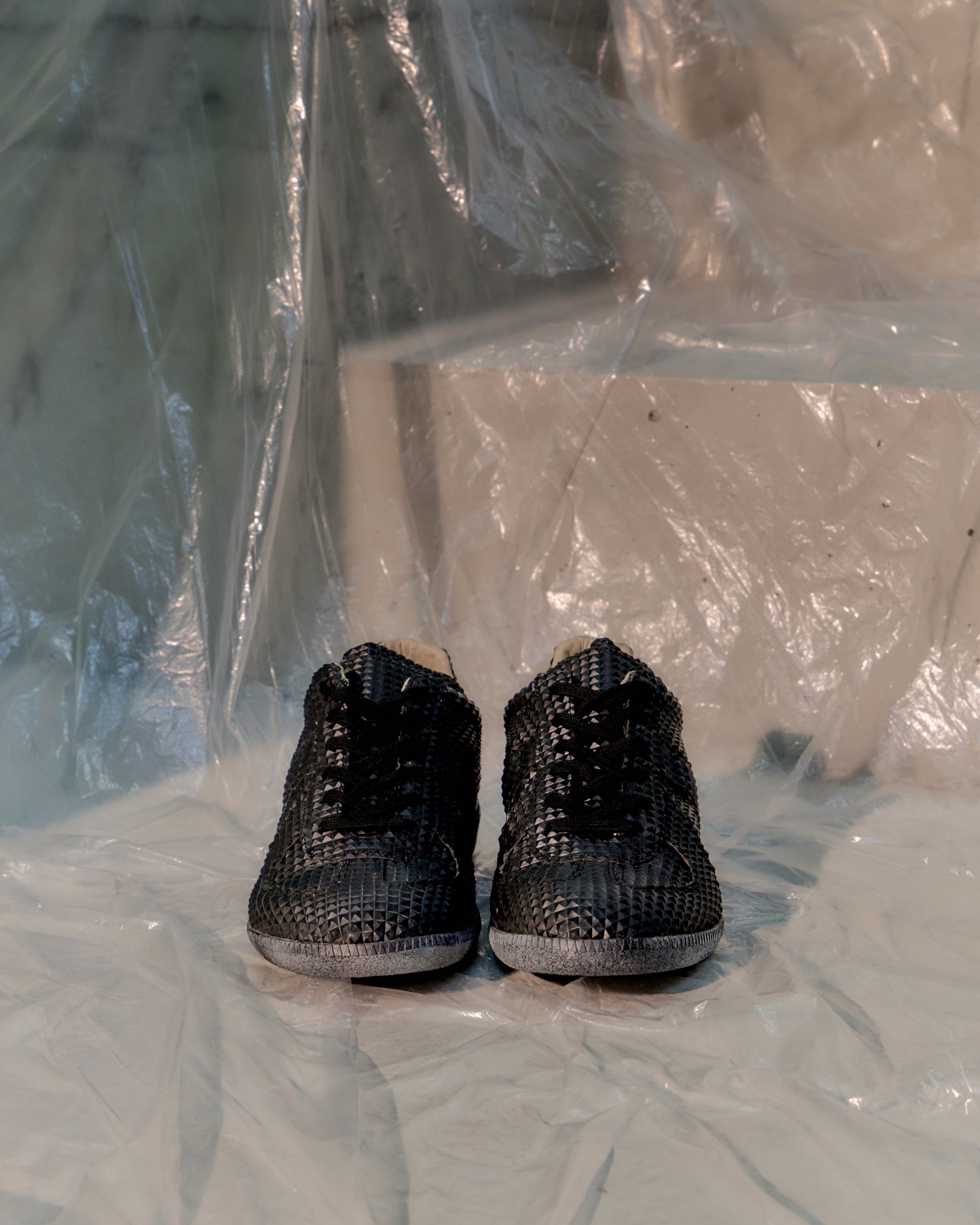 Black textured Maison Margiela sneakers on a light-coloured floor with plastic sheeting in the background