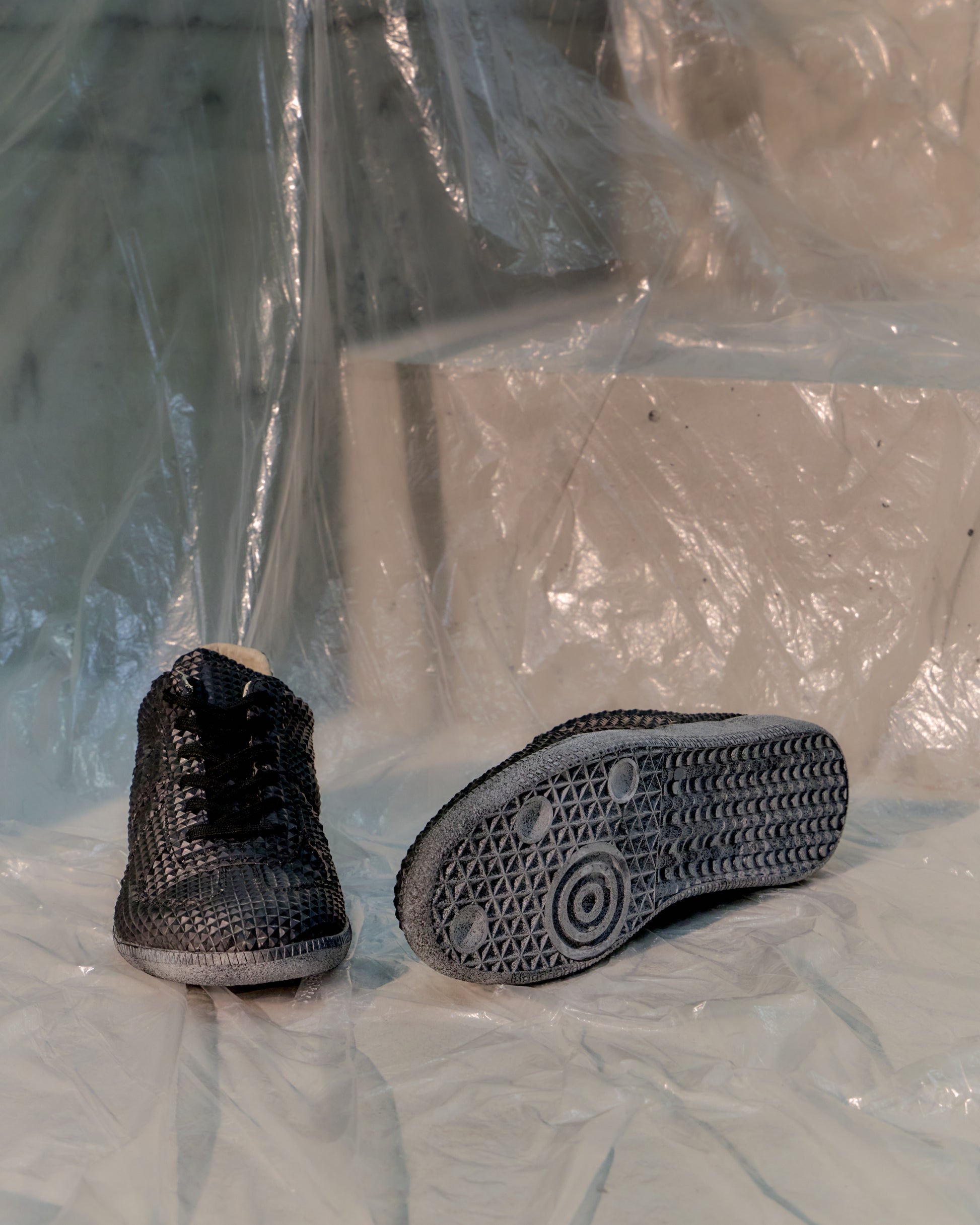Black textured Maison Margiela shoes on a white surface with a clear plastic sheet in the background