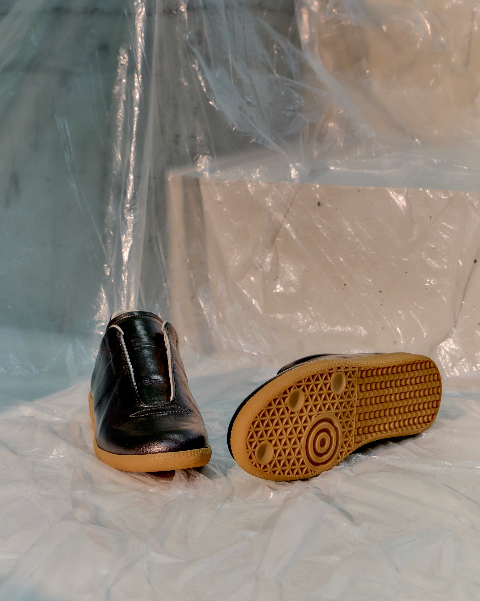 Black Maison Margiela shoe with brown sole on a white surface with plastic wrap in the background