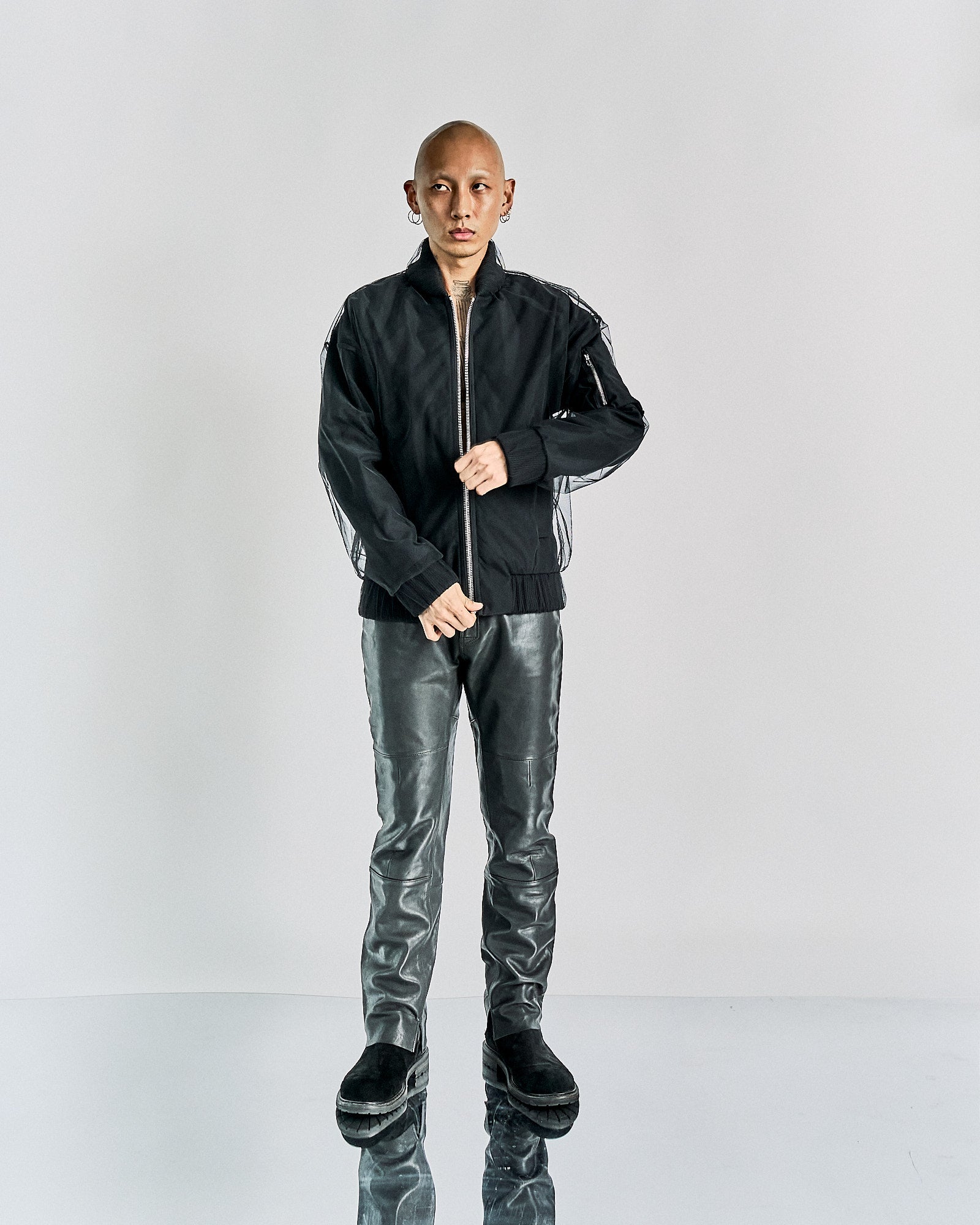 A person stands confidently wearing a black Maison Margiela jacket and shiny silver pants against a plain background.