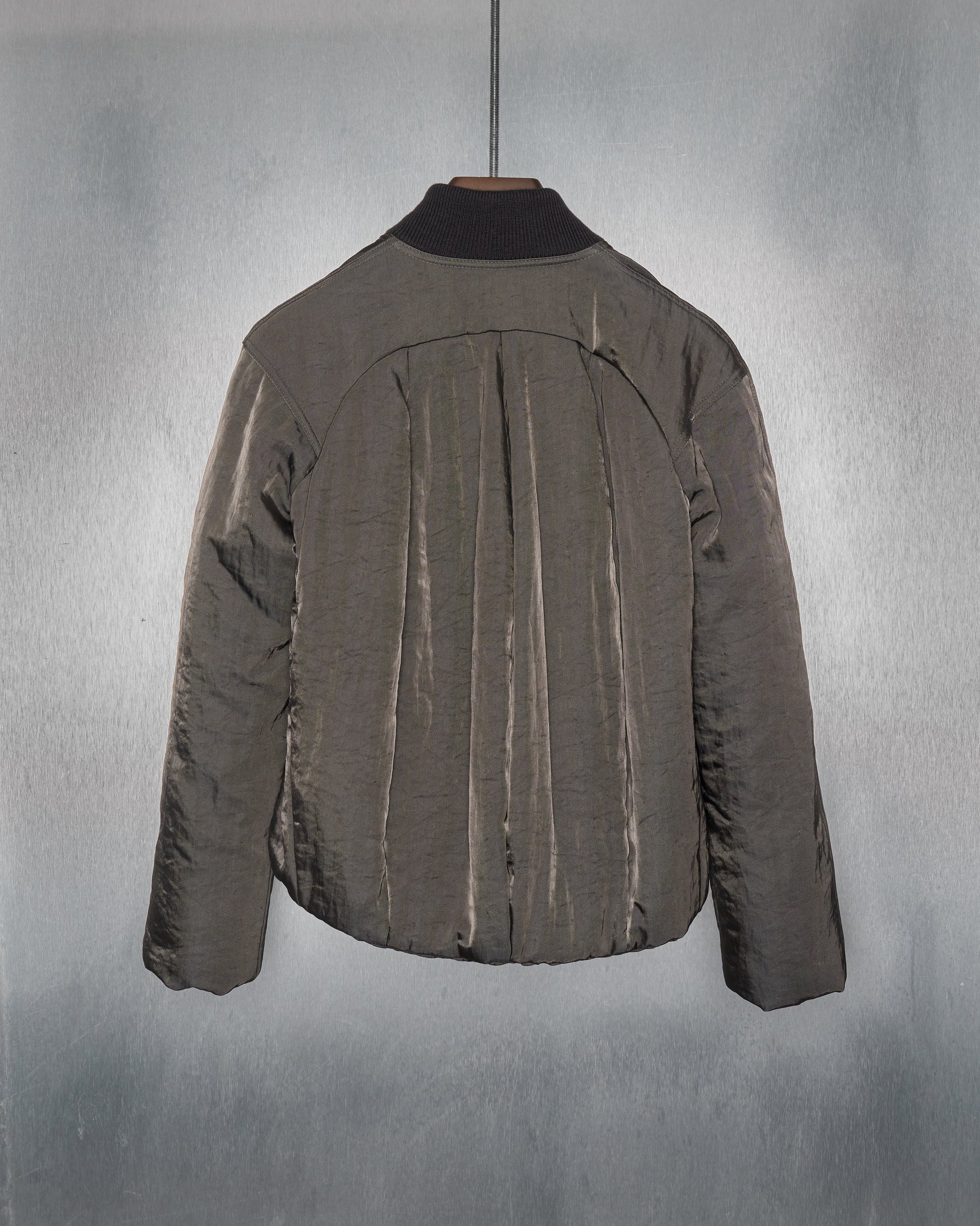A Maison Margiela jacket is hanging on a wooden hanger against a textured grey background. The jacket features vertical pleats and a black collar