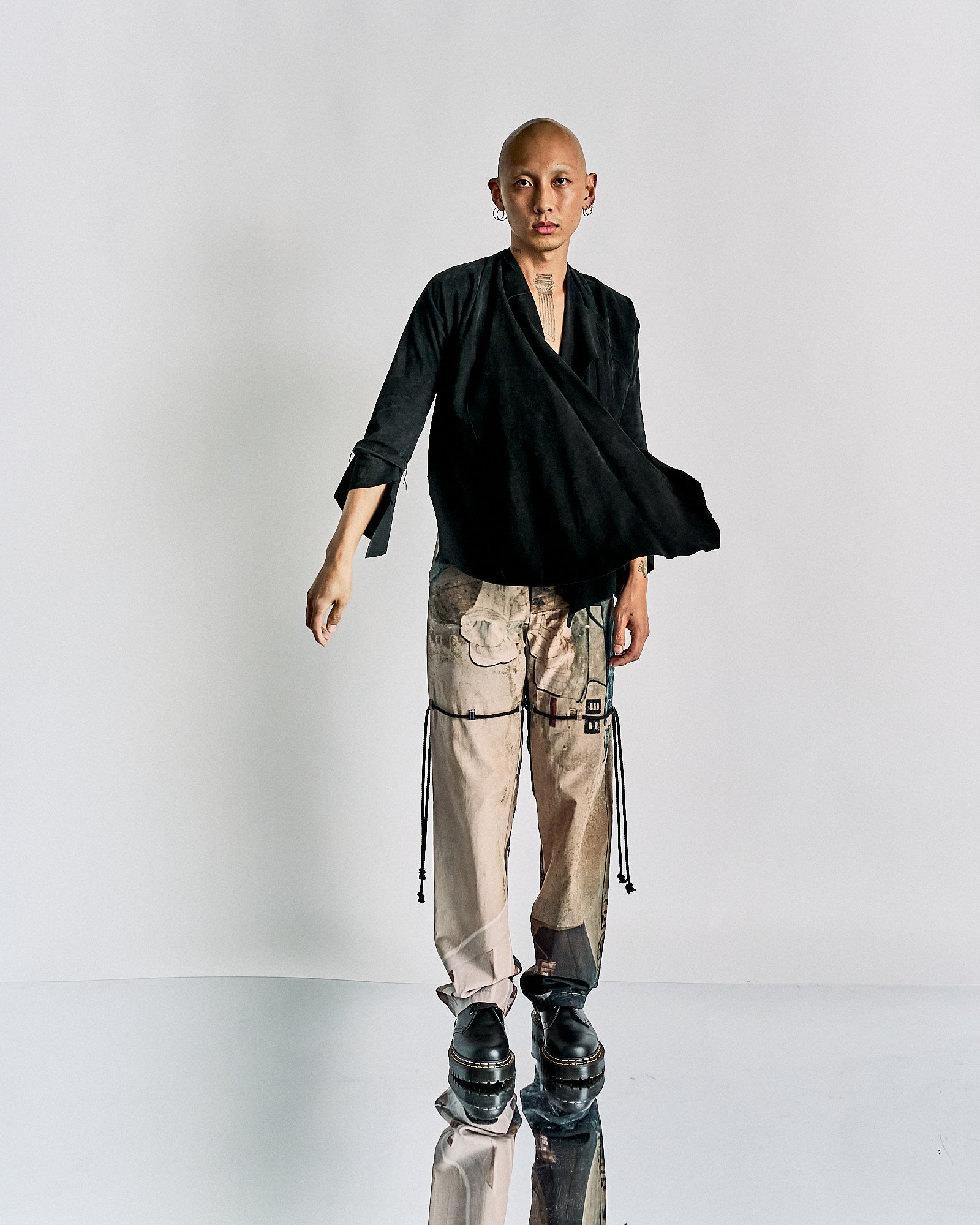 Bald individual wearing a black Maison Margiela jacket and beige cargo pants with black detailing.