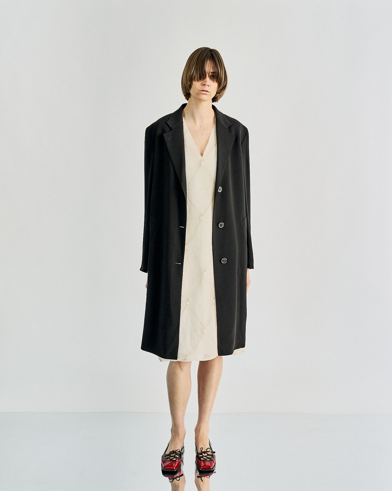 Fashionable individual in a black Maison Margiela coat over a cream quilted dress, red and black patent shoes. 