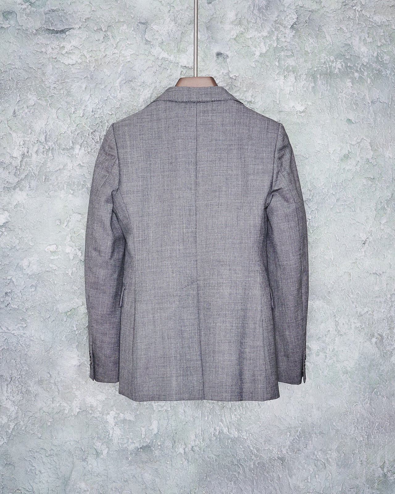 A gray wool Maison Margiela blazer with notch lapel and single button closure, displayed on a hanger against a textured background.