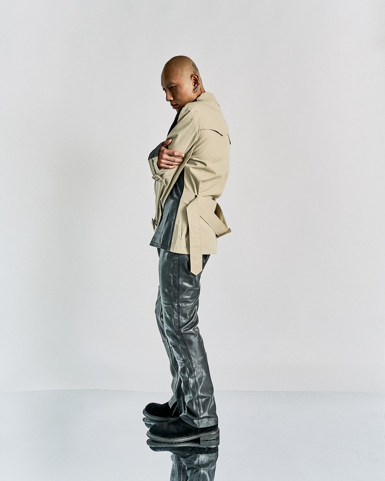 A male model wearing a Maison Margiela leather front zip jacket in black and beige, with a camp-collar and front zip closure, standing in a studio setting.