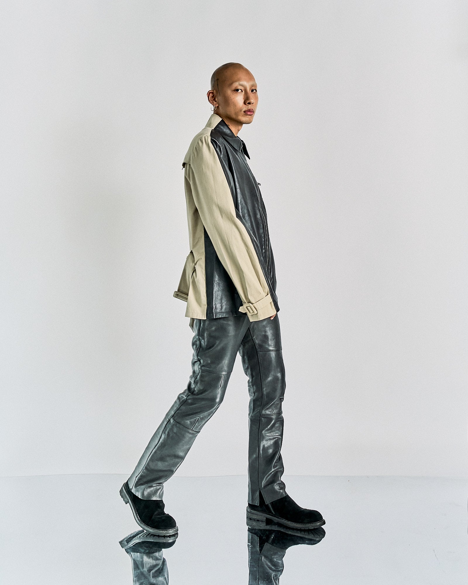 A person walks confidently, wearing a stylish beige and black Maison Margiela jacket with matching leather pants.