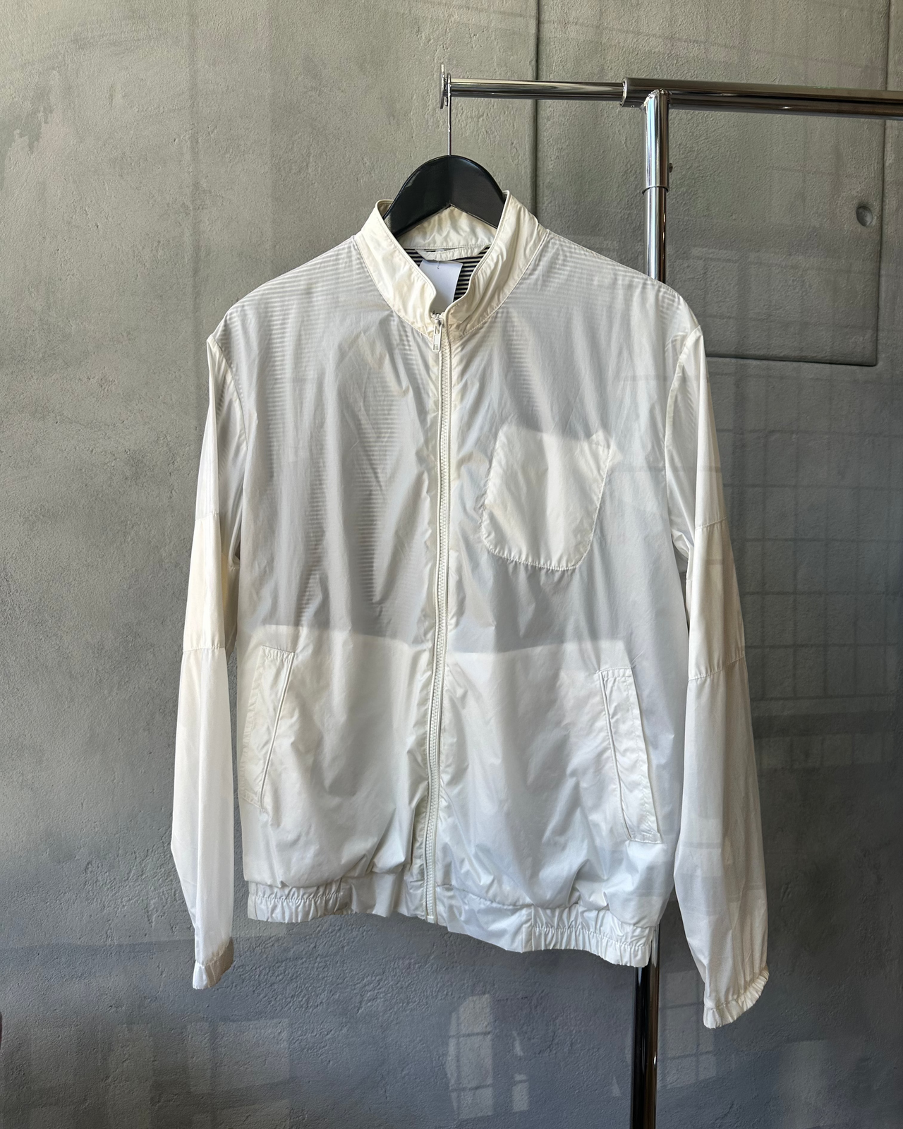 White Maison Margiela jacket on a hanger against a gray concrete wall