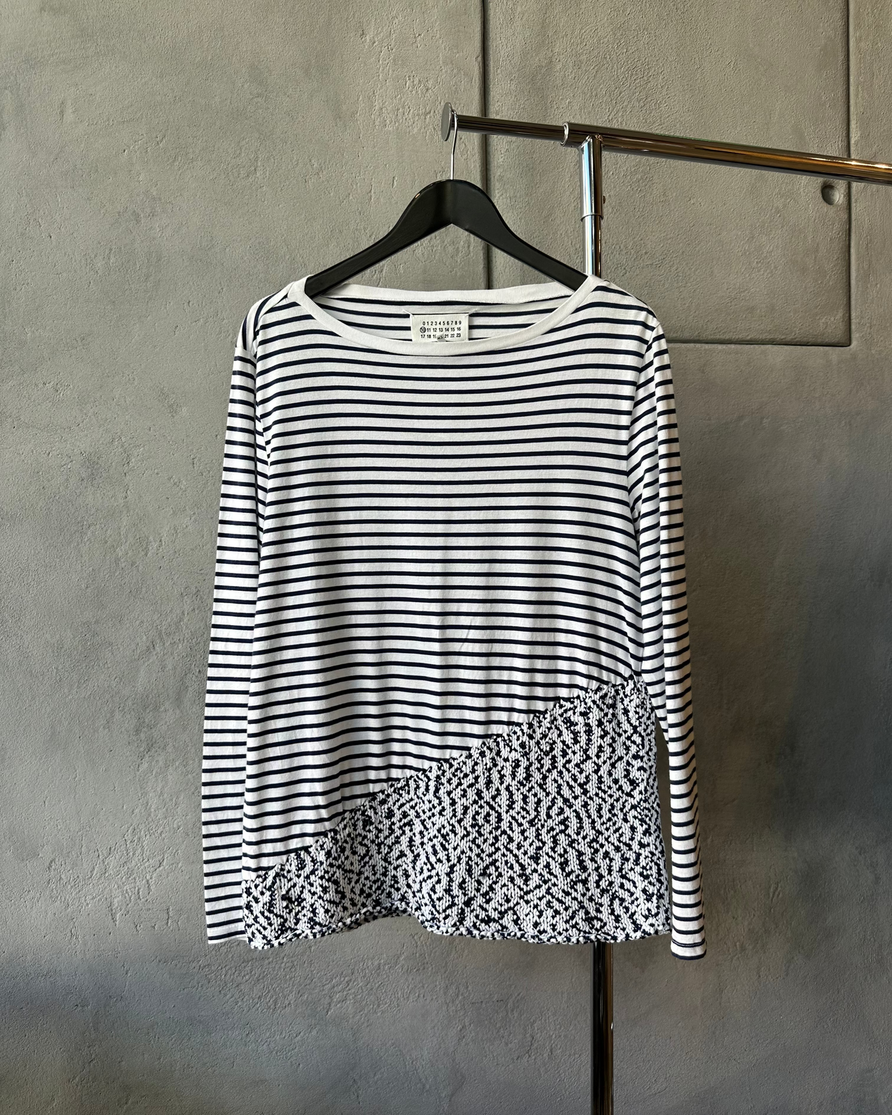 Blue and white striped Maison Margiela shirt with a floral pattern on a hanger against a gray wall.