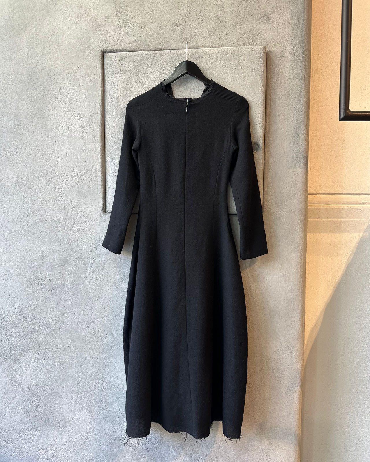 Black Marc Le Bihan dress hanging on a hanger against a neutral wall.
