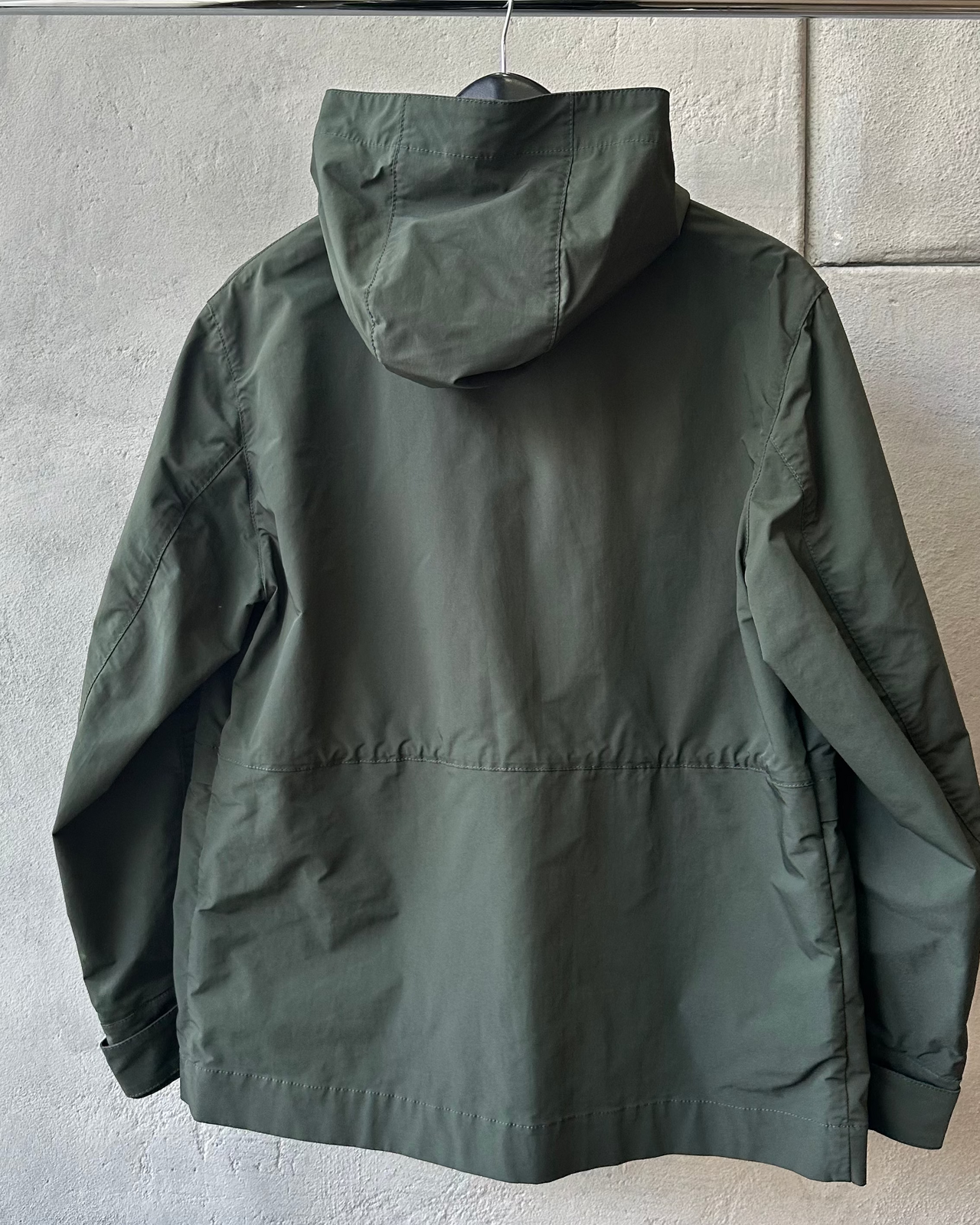 Green Marni raincoat hanging on a rack against a gray wall