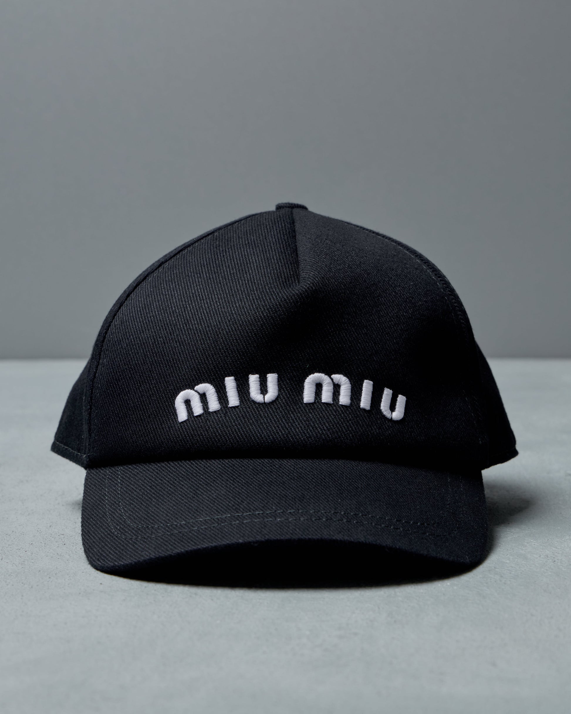 Black cap with 'miu miu' branding on a gray background