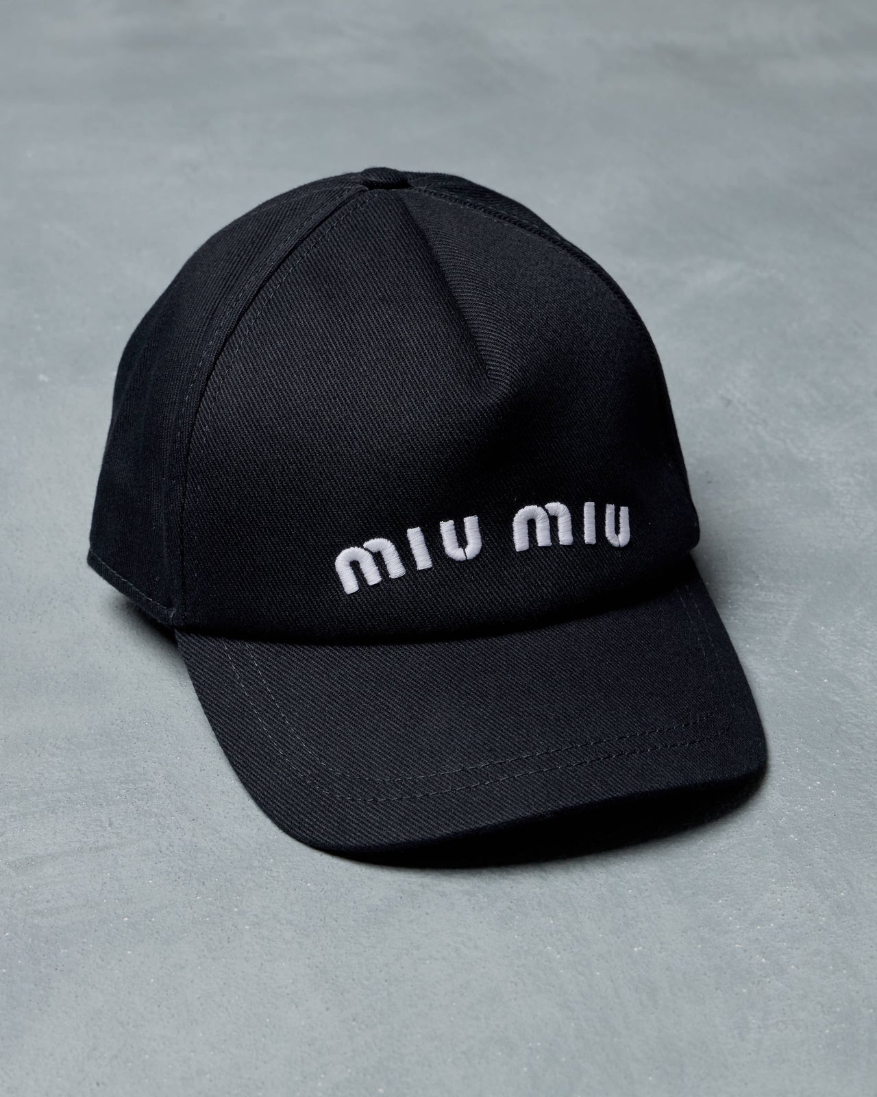 Black cap with 'miu miu' branding on a gray background