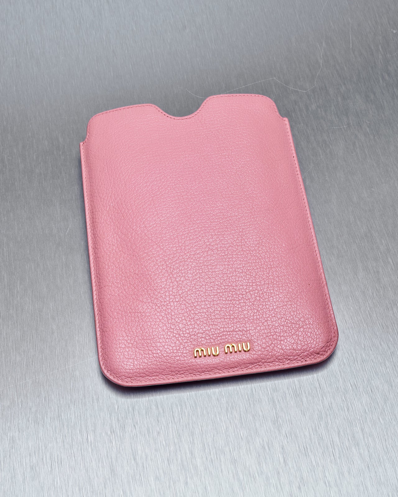 A pink Miu Miu leather iPad mini sleeve with gold studded branding and tonal stitching.