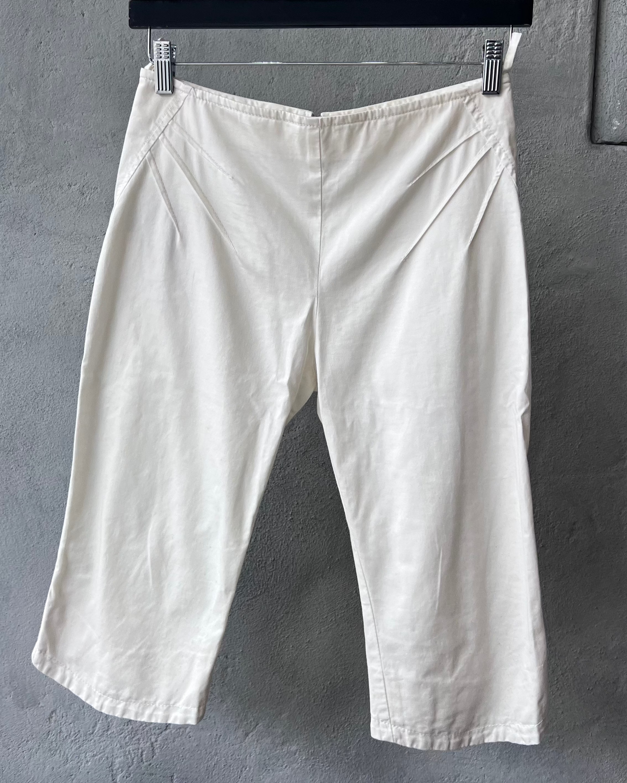 White Miumiu pants hanging on a rack against a gray wall