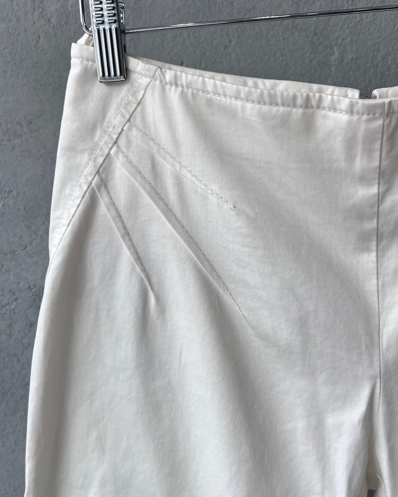 White Miumiu pants hanging on a rack against a gray wall