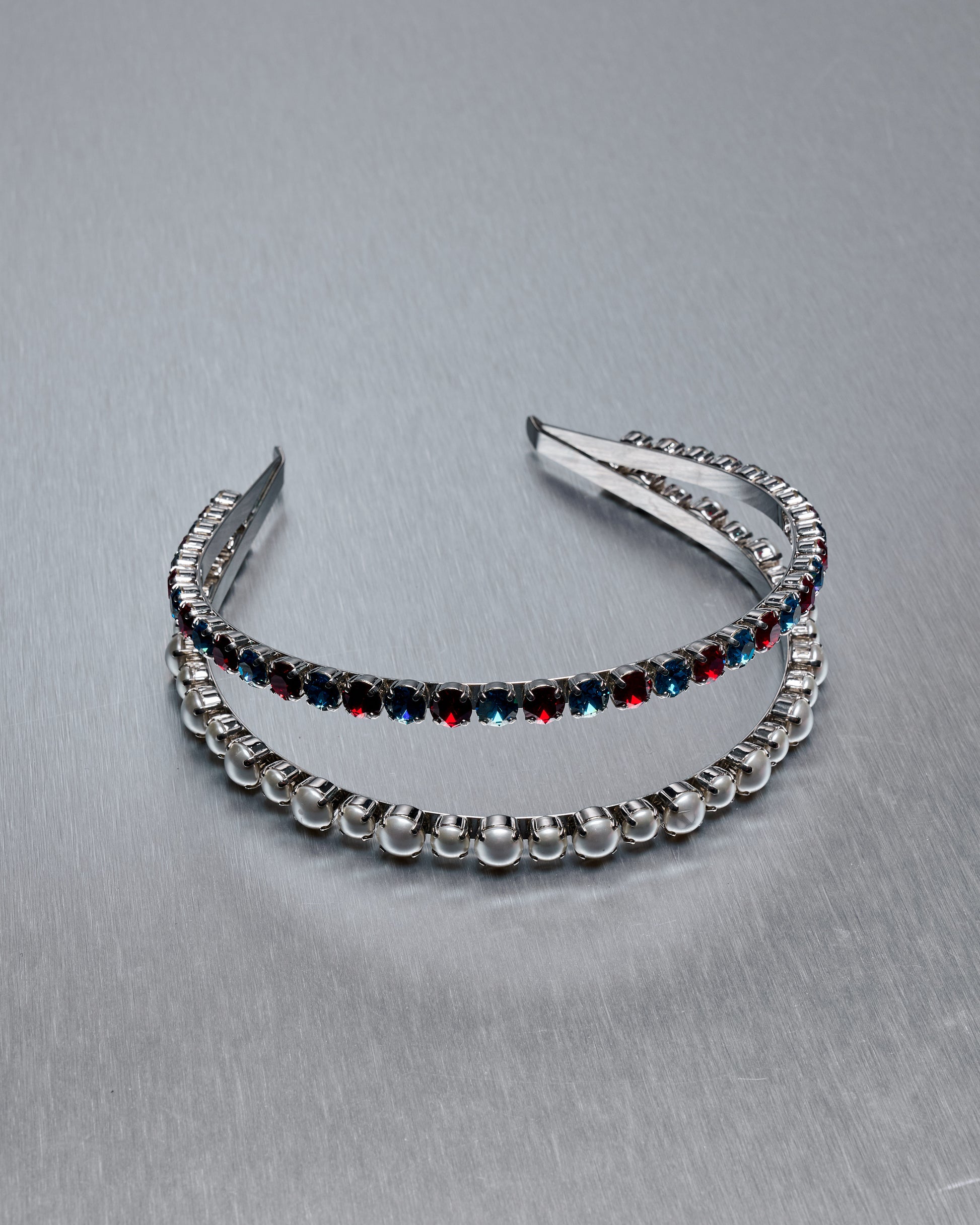 A double Miu Miu headband with one band featuring pearl-like beads and the other with glass gems, both in a mirror-finished metal.