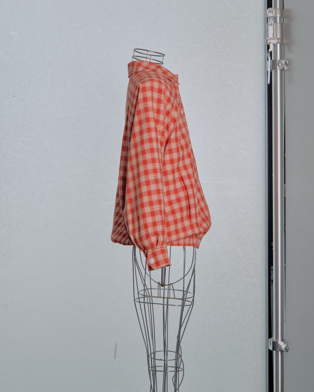 Red and white checkered Miu Miu bomber jacket on a wire mannequin against a gray background