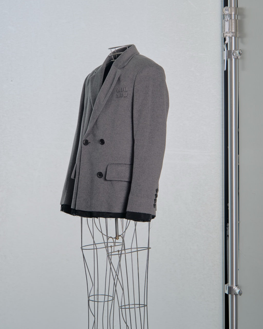 Gray double-breasted  Miu Miu jacket on a mannequin against a light gray background