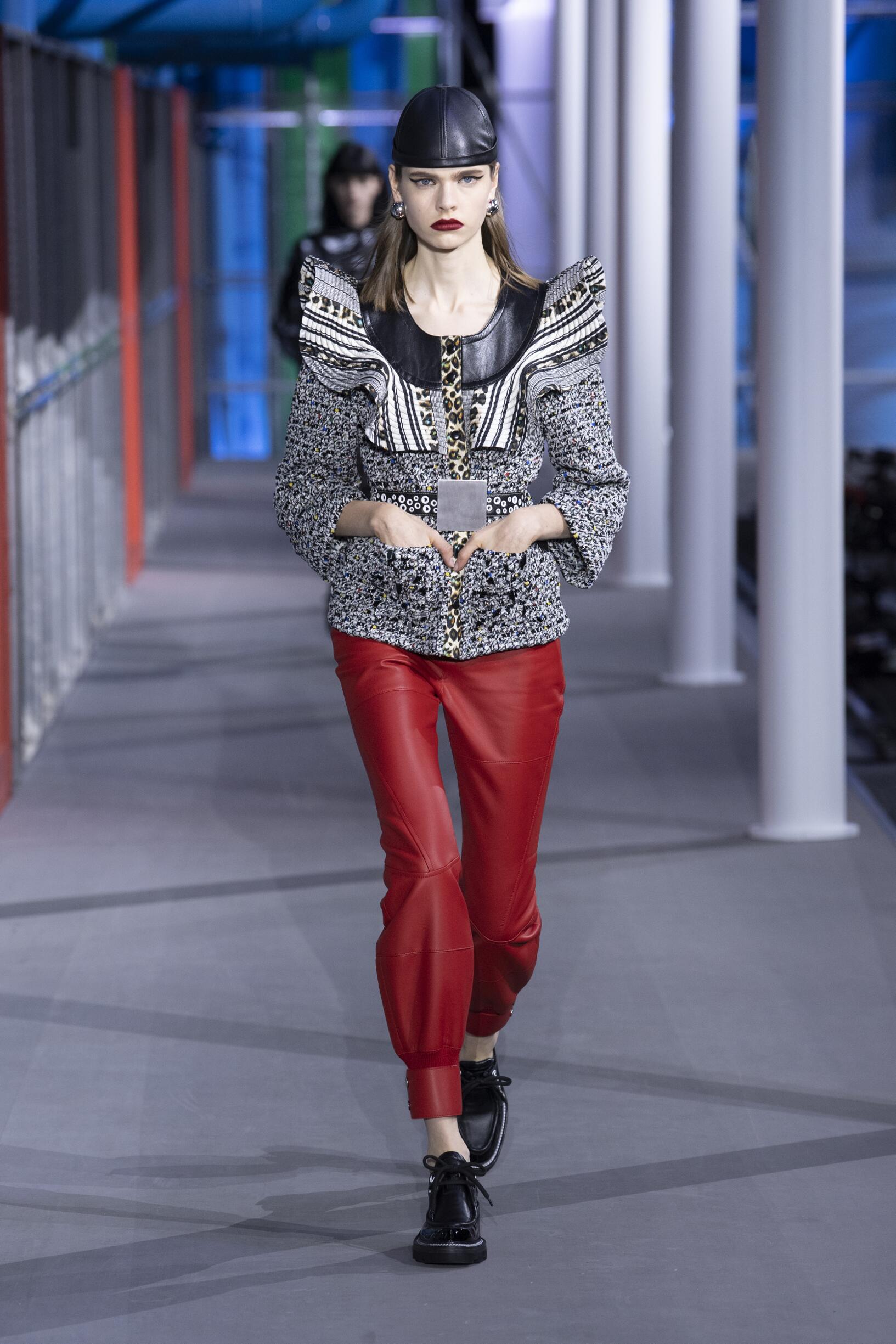 Model walking on a Louis Vuitton runway wearing a patterned top, red pants, and black shoes.